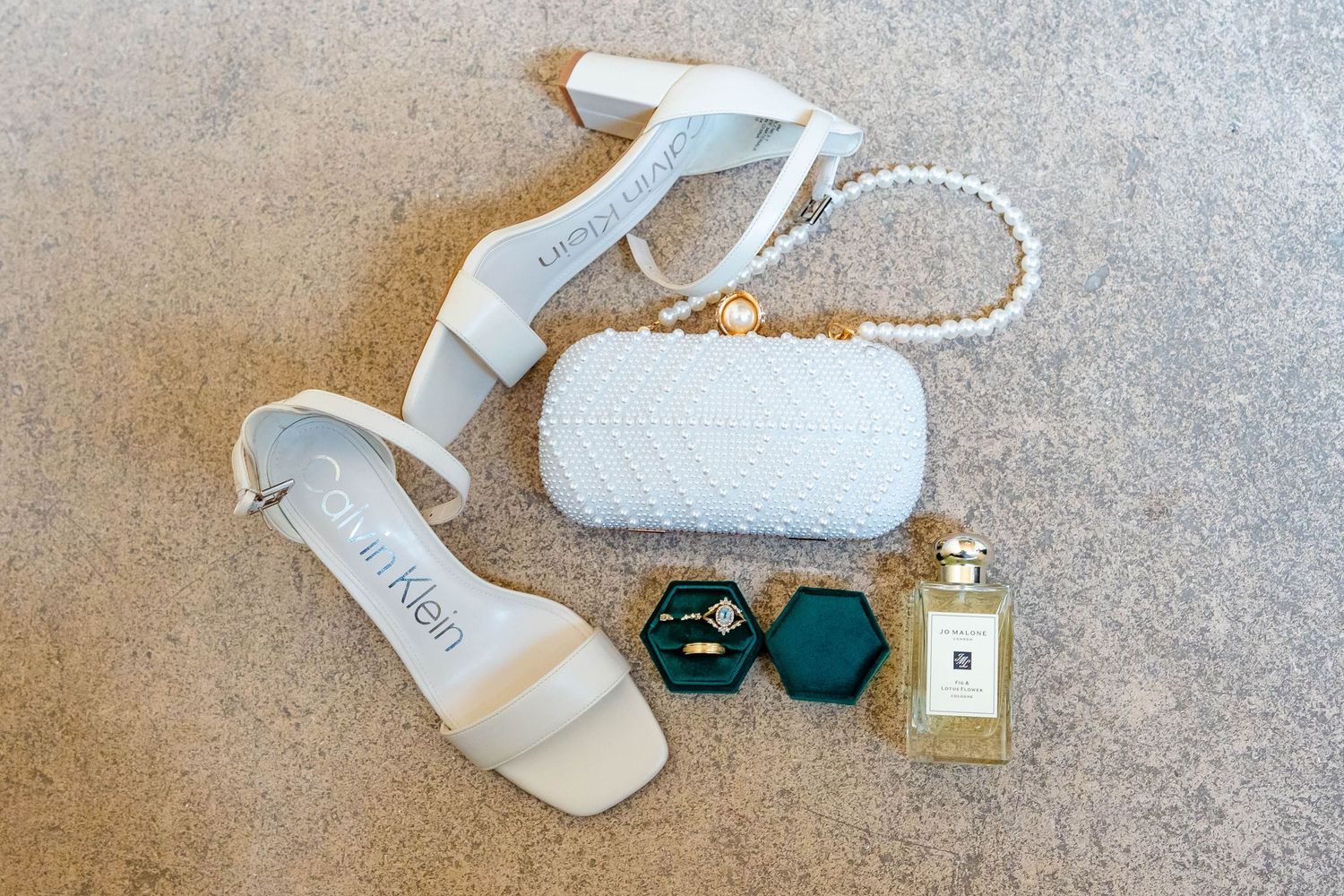 White leather ankle boots with pearl straps and gold hardware displayed on a beige textured surface.