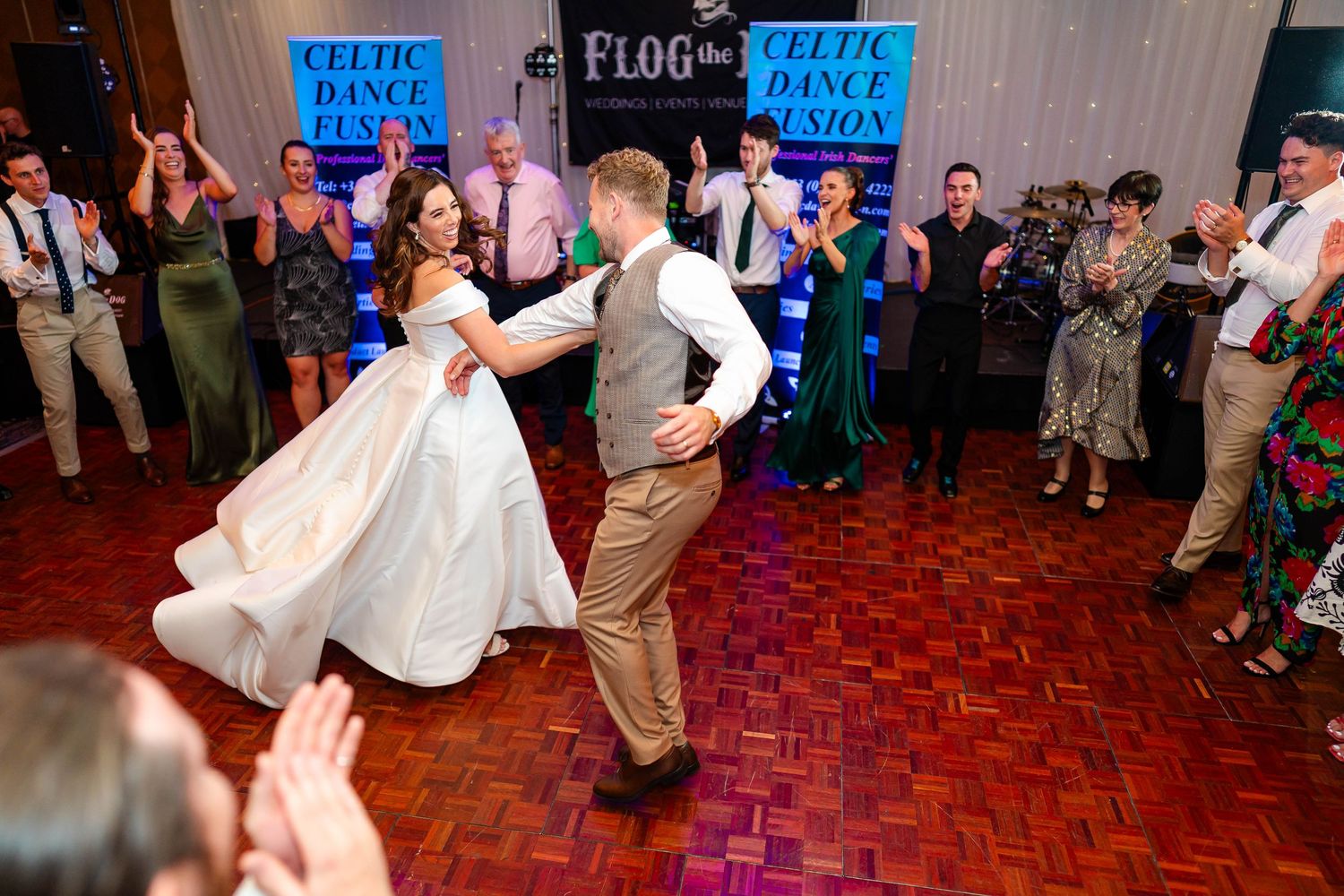 Wedding couple dances surrounded by guests on a red dance floor at their reception celebration.