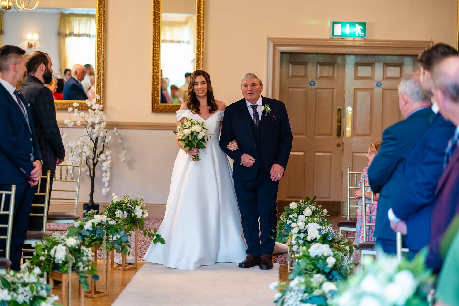 Wedding ceremony processional in elegant venue with floral aisle decorations.