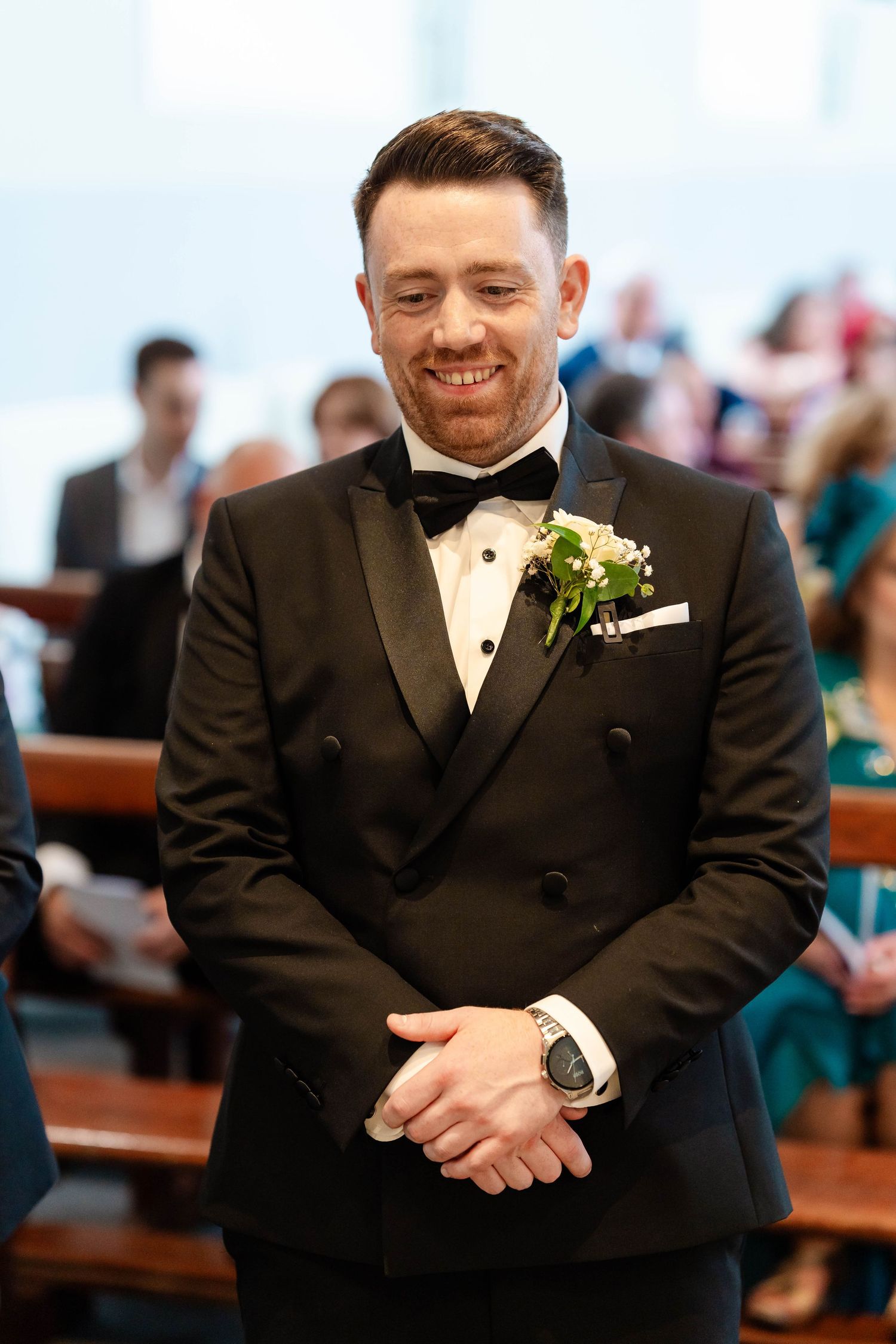 Groom in classic black tuxedo smiling during wedding ceremony.