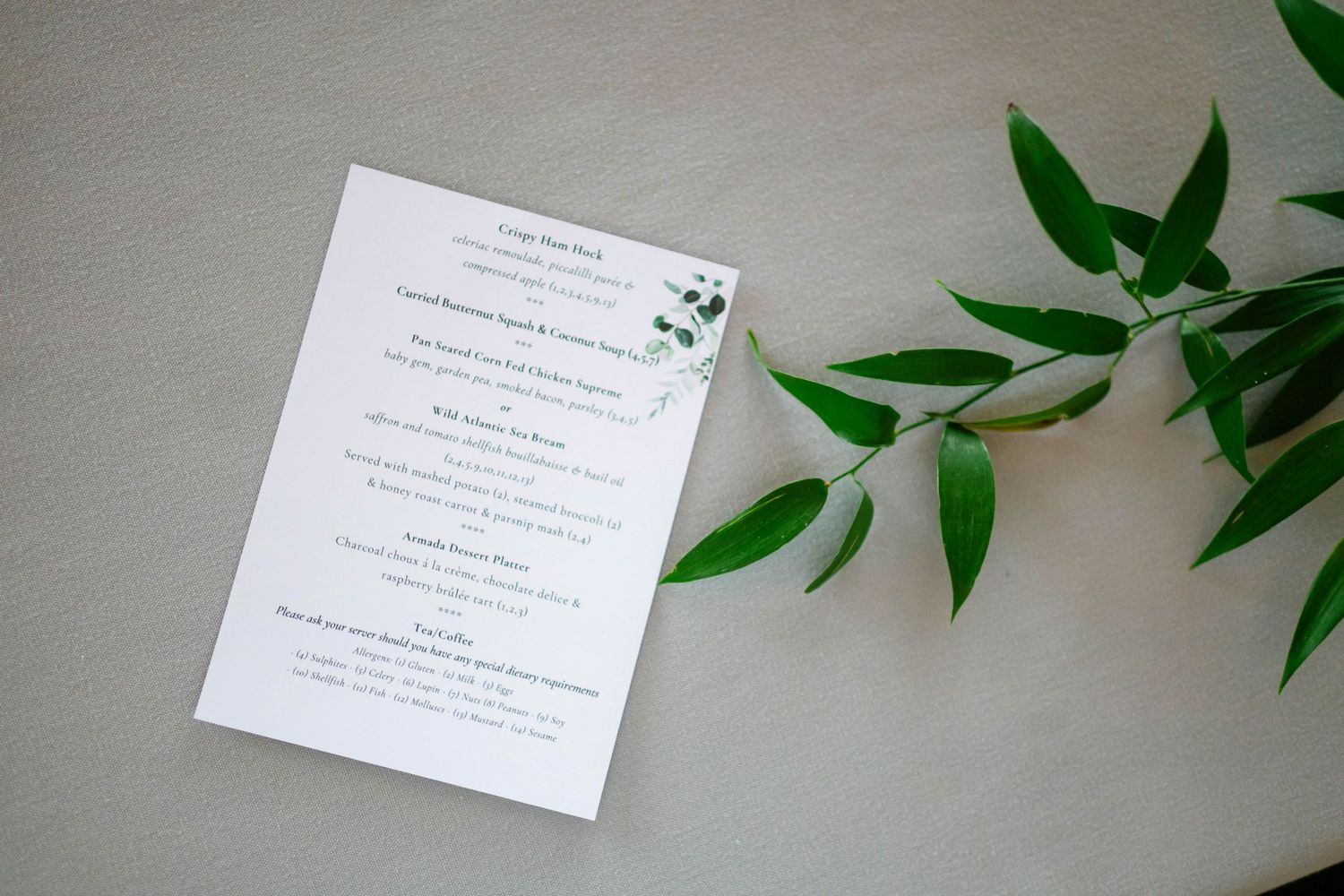 Detailed wedding menu card with greenery accents on light background.