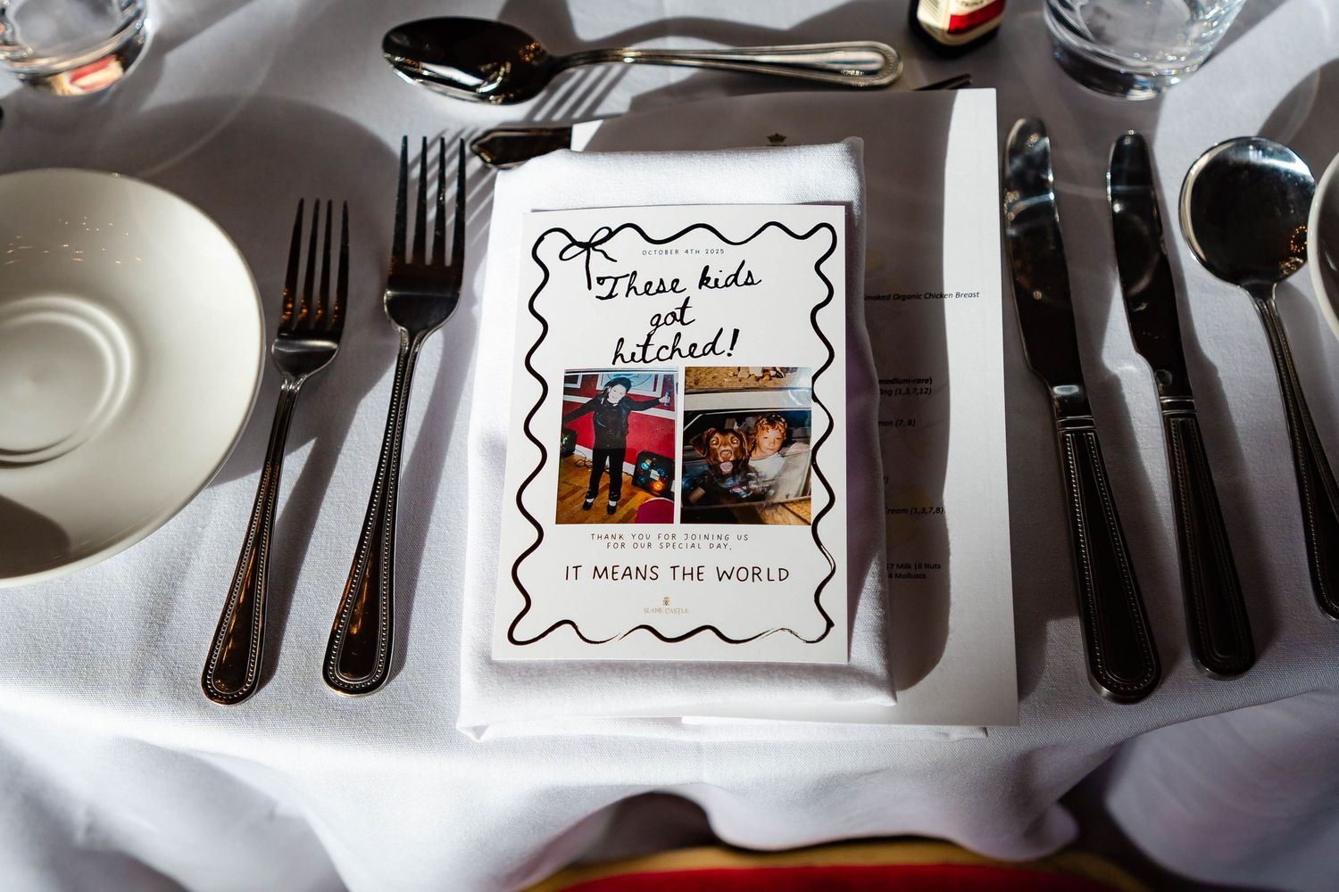 Place settings at a formal dinner table with black cutlery and white plates on a white tablecloth.