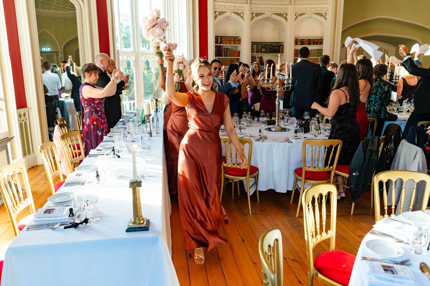 Wedding reception guests mingle and dine in an elegant venue with white tablecloths and rustic wooden details.