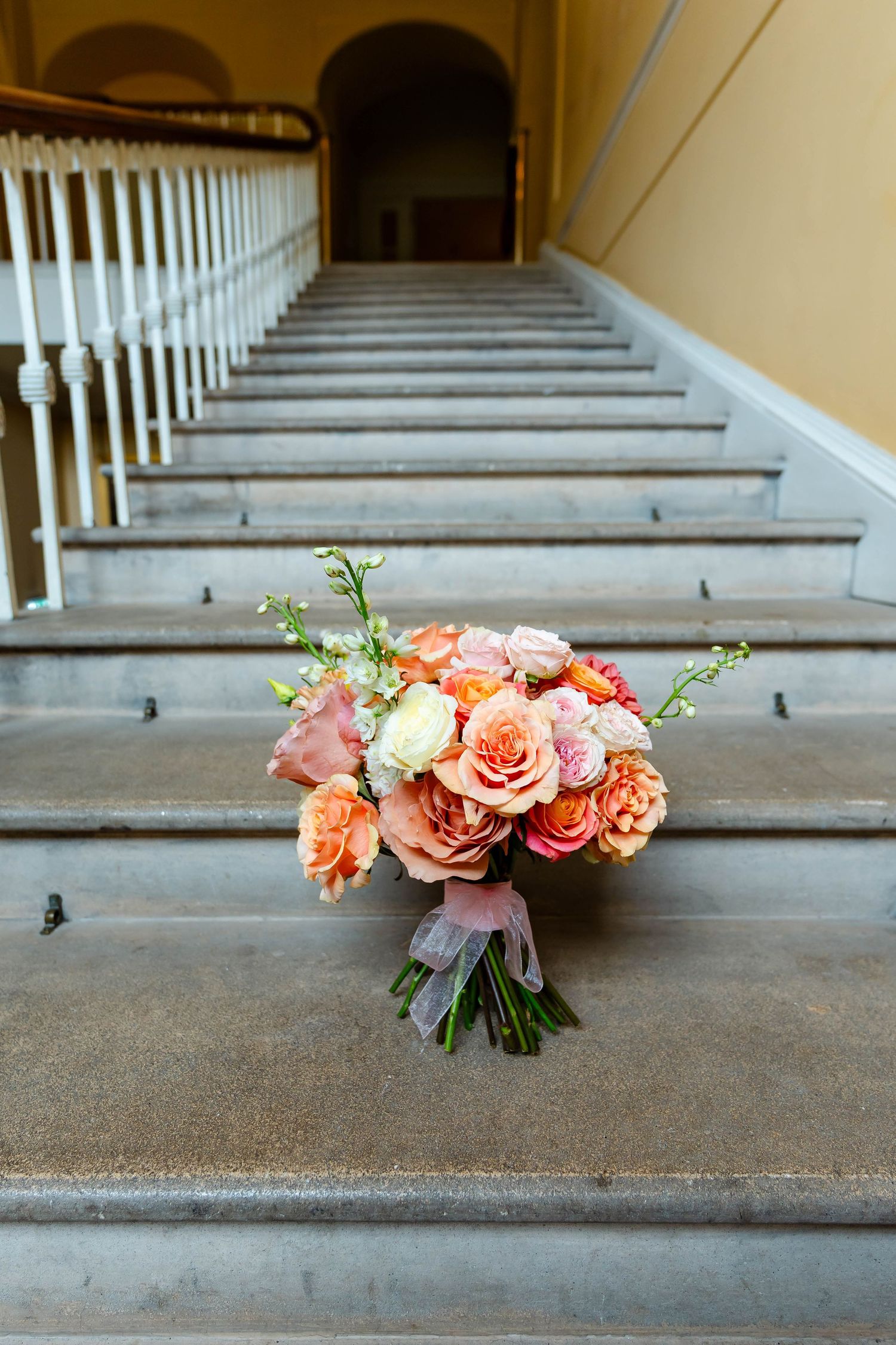 A beautiful peach and coral rose bouquet sits on concrete steps in a series of similar styled photographs.