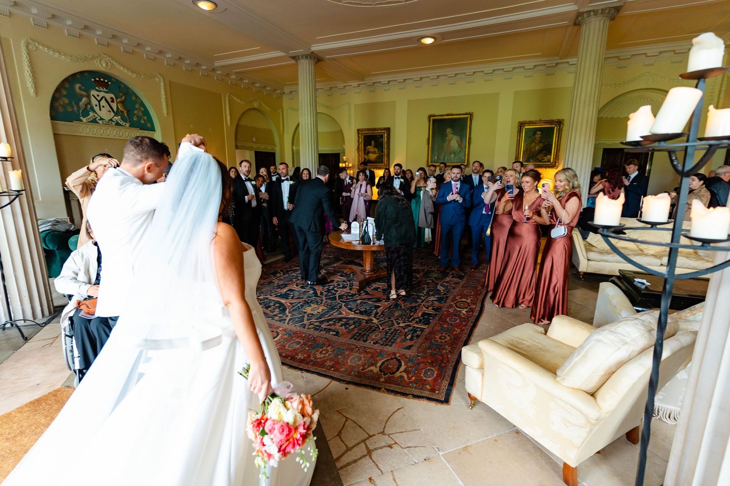 Wedding guests gather in an elegant yellow ballroom with ornate decor and a large oriental rug during a reception.
