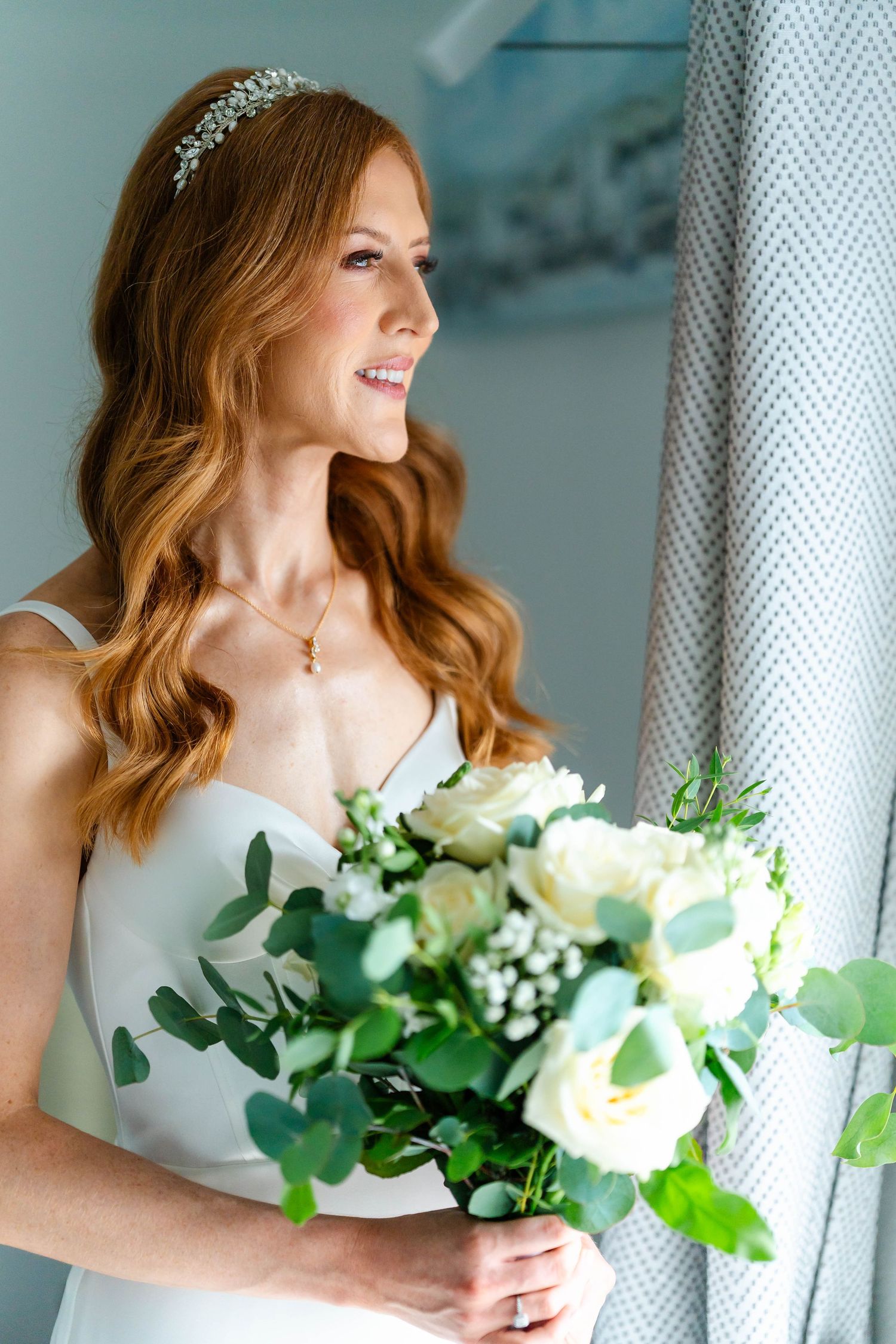 An elegant white wedding bouquet with roses and greenery held by someone in white.