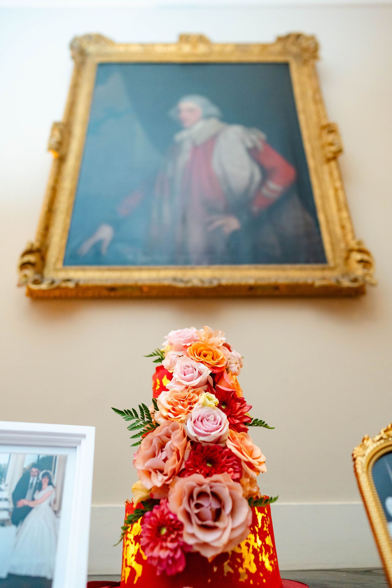 Elegant floral centerpiece with pink and peach roses displayed against a wall with ornate gold-framed artwork.