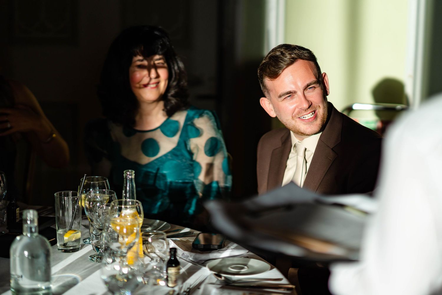 Wedding guests enjoy dinner and conversation at an elegant reception table with wine glasses and place settings.