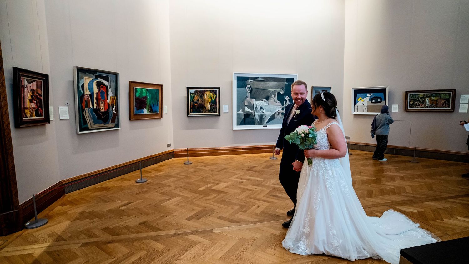 Panoramic view of a modern art gallery with white walls and herringbone wood flooring.