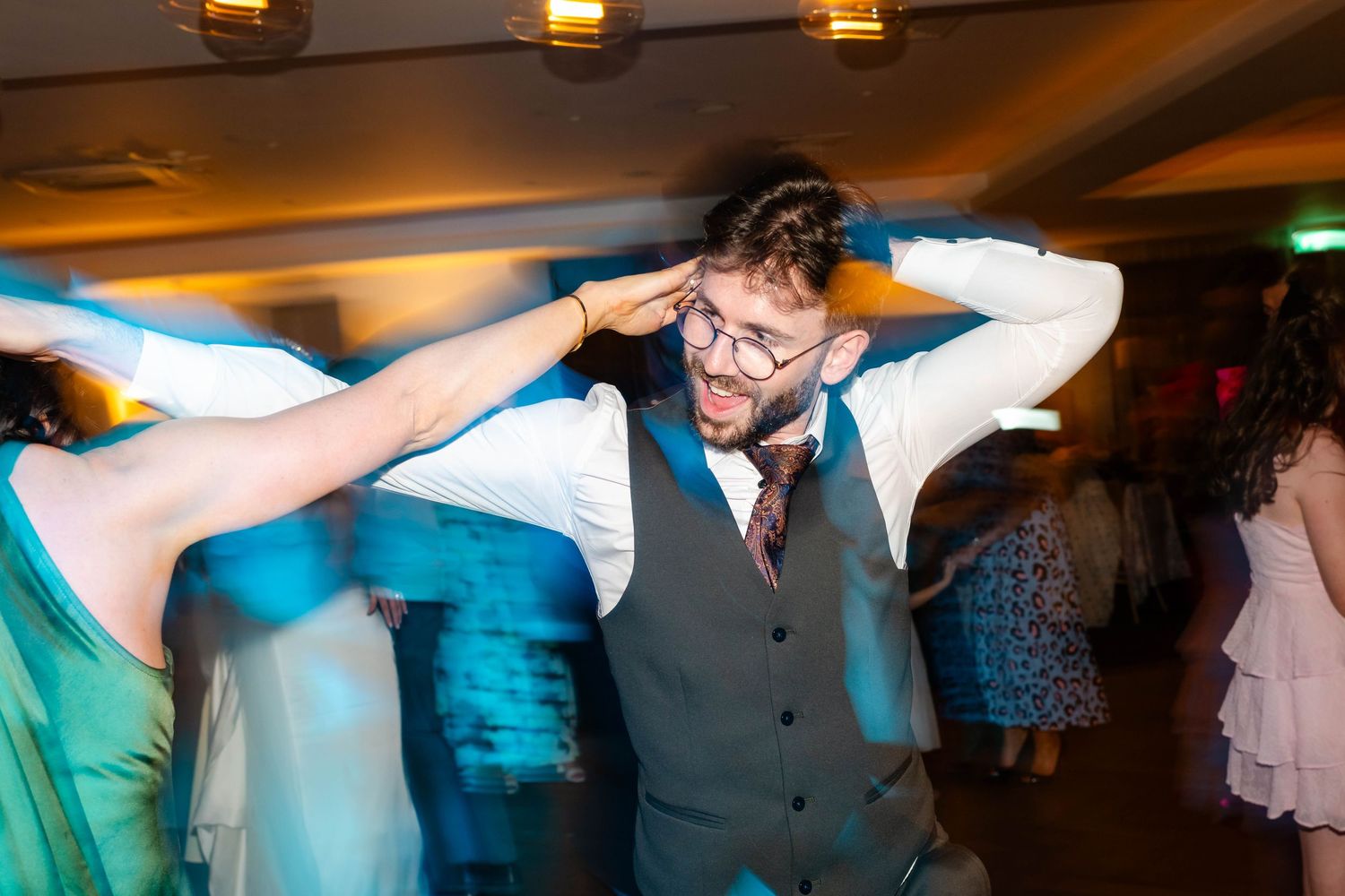 Guests performing synchronized dance moves at a wedding reception with blue lighting effects.