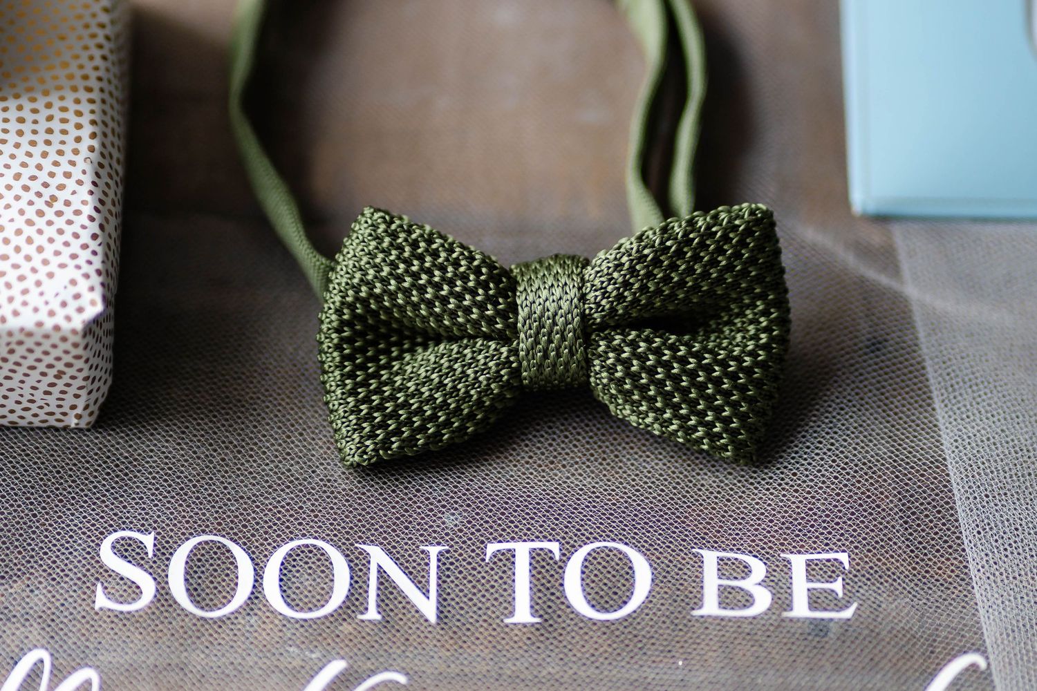 Wedding details including green polka dot bow tie and white accessories laid on turquoise surface.