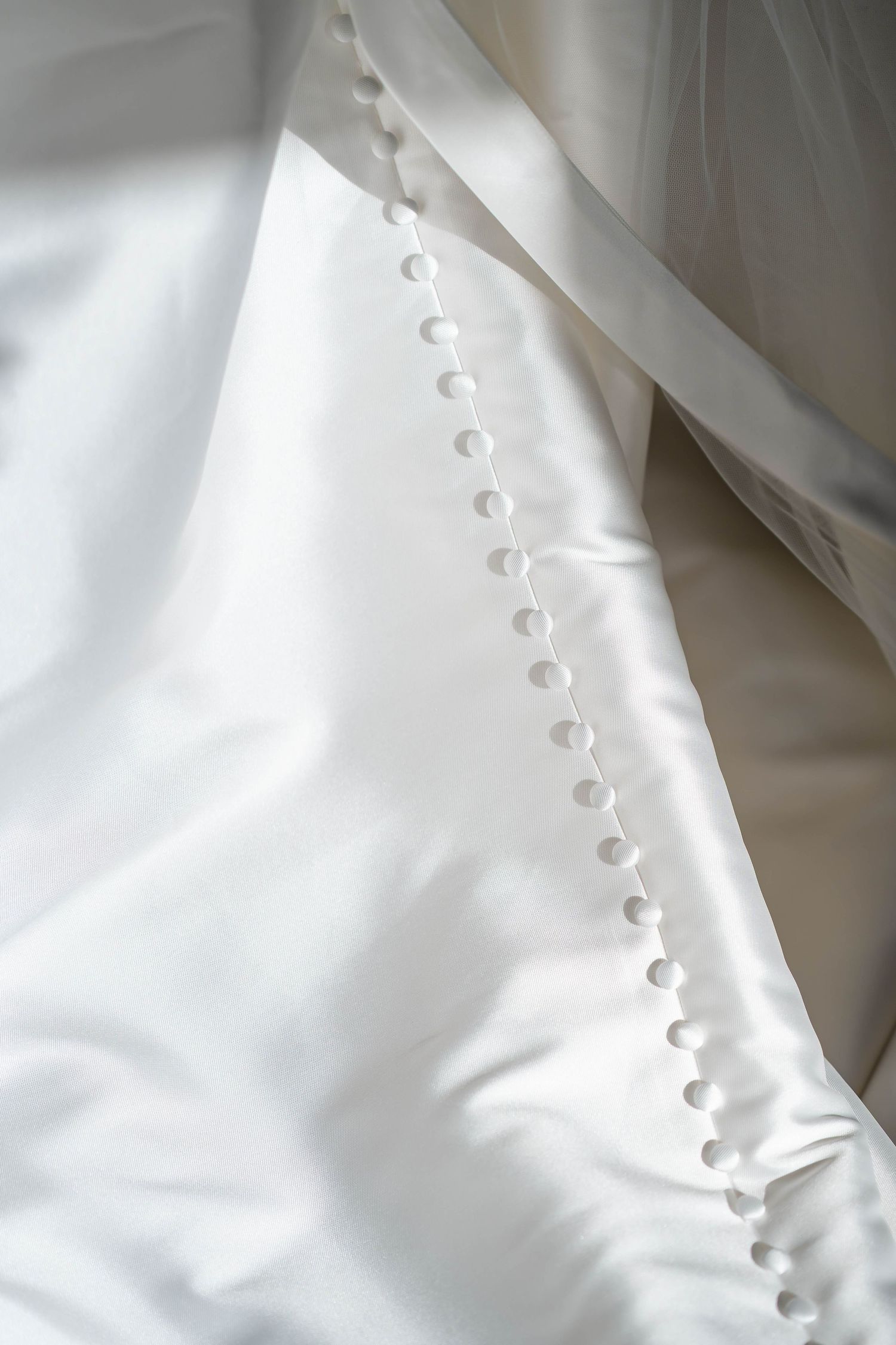 Close-up detail of white wedding dress fabric with delicate button closures and soft folds.