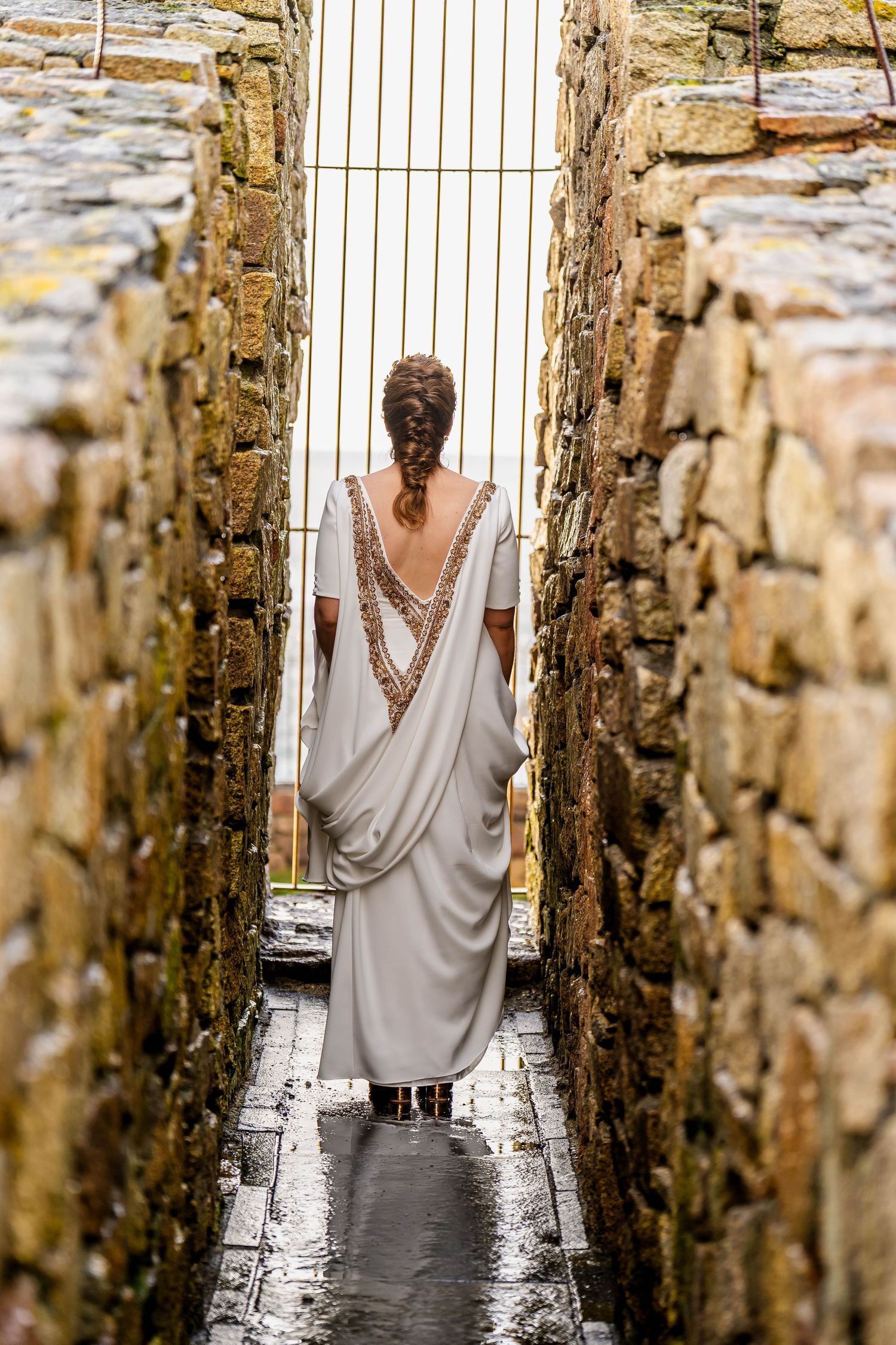 White wedding dress detail shot through stone archways in an ancient corridor.