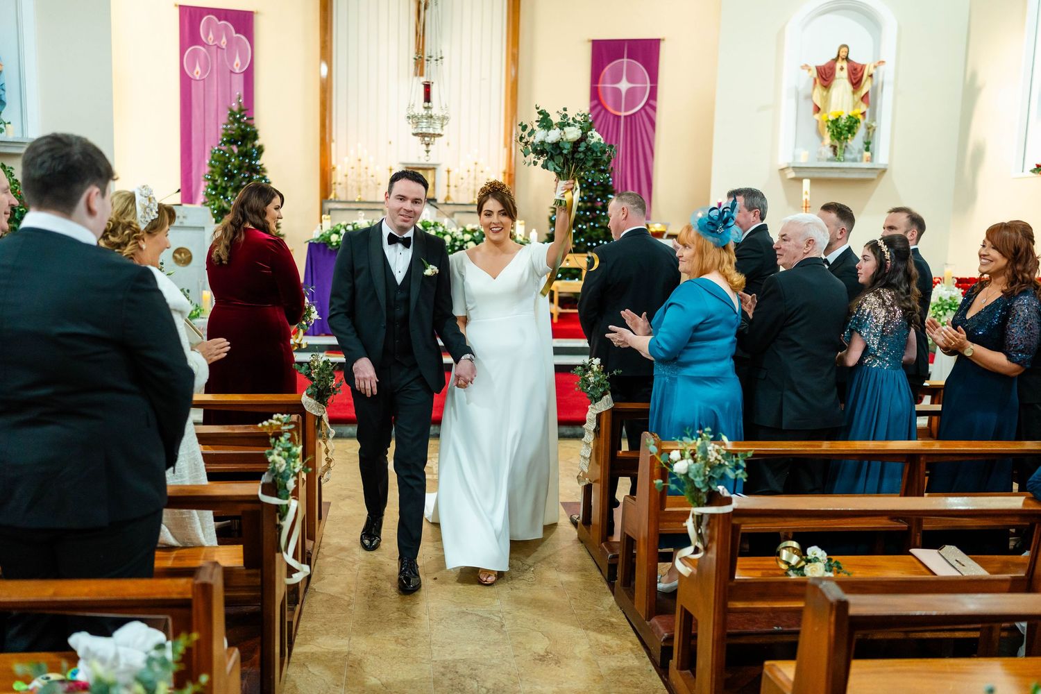 Wedding guests seated in wooden pews during church ceremony with holiday decorations.