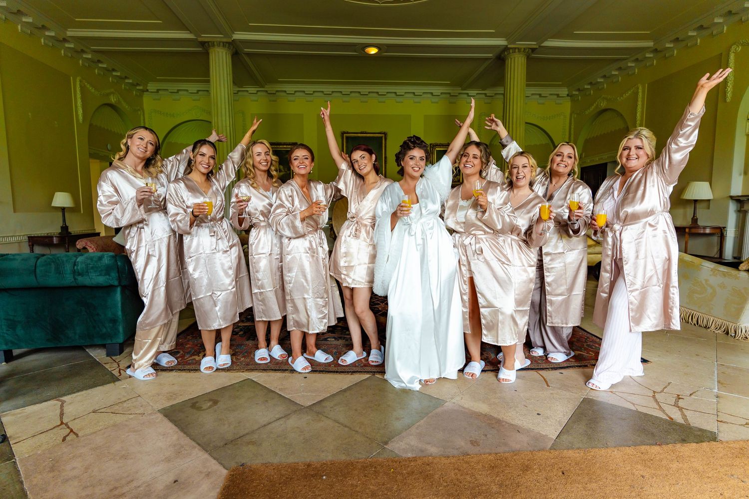 A group in matching champagne silk robes pose together joyfully during a wedding celebration in an elegant venue.