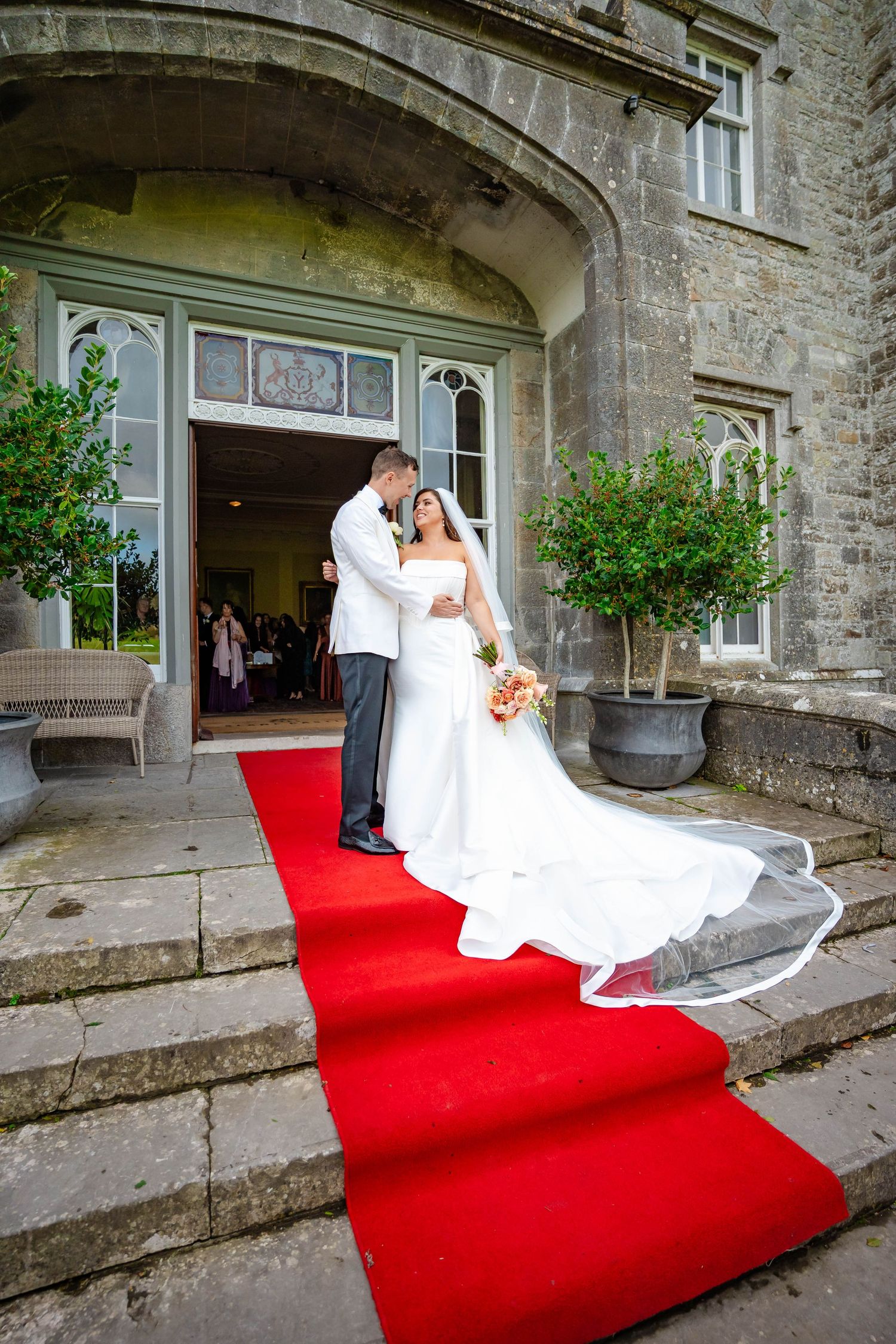 A romantic wedding couple poses on red carpet steps at a historic stone building in a sequence of five photos.