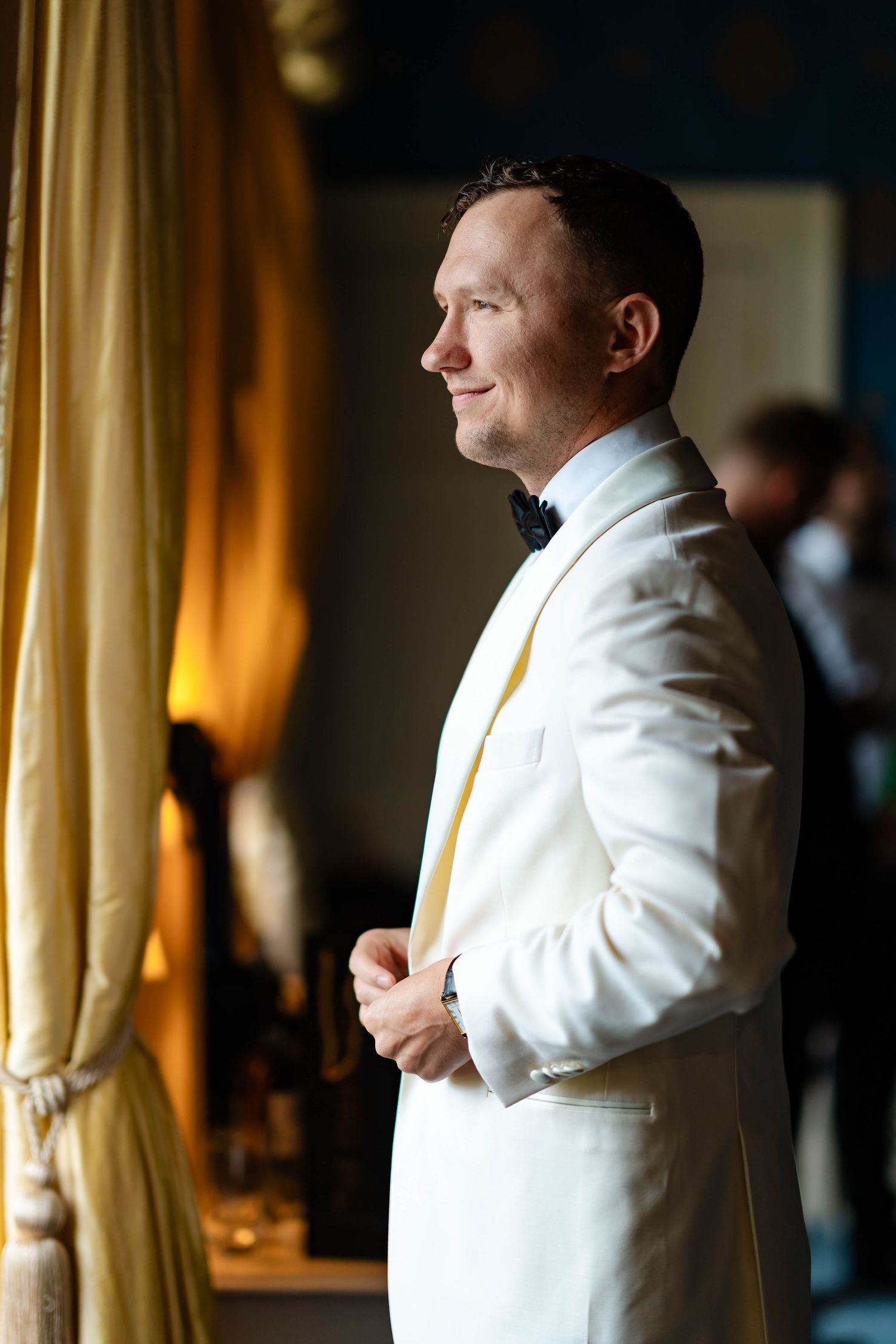 A person in a white tuxedo jacket adjusts their tie while getting ready for a formal event.
