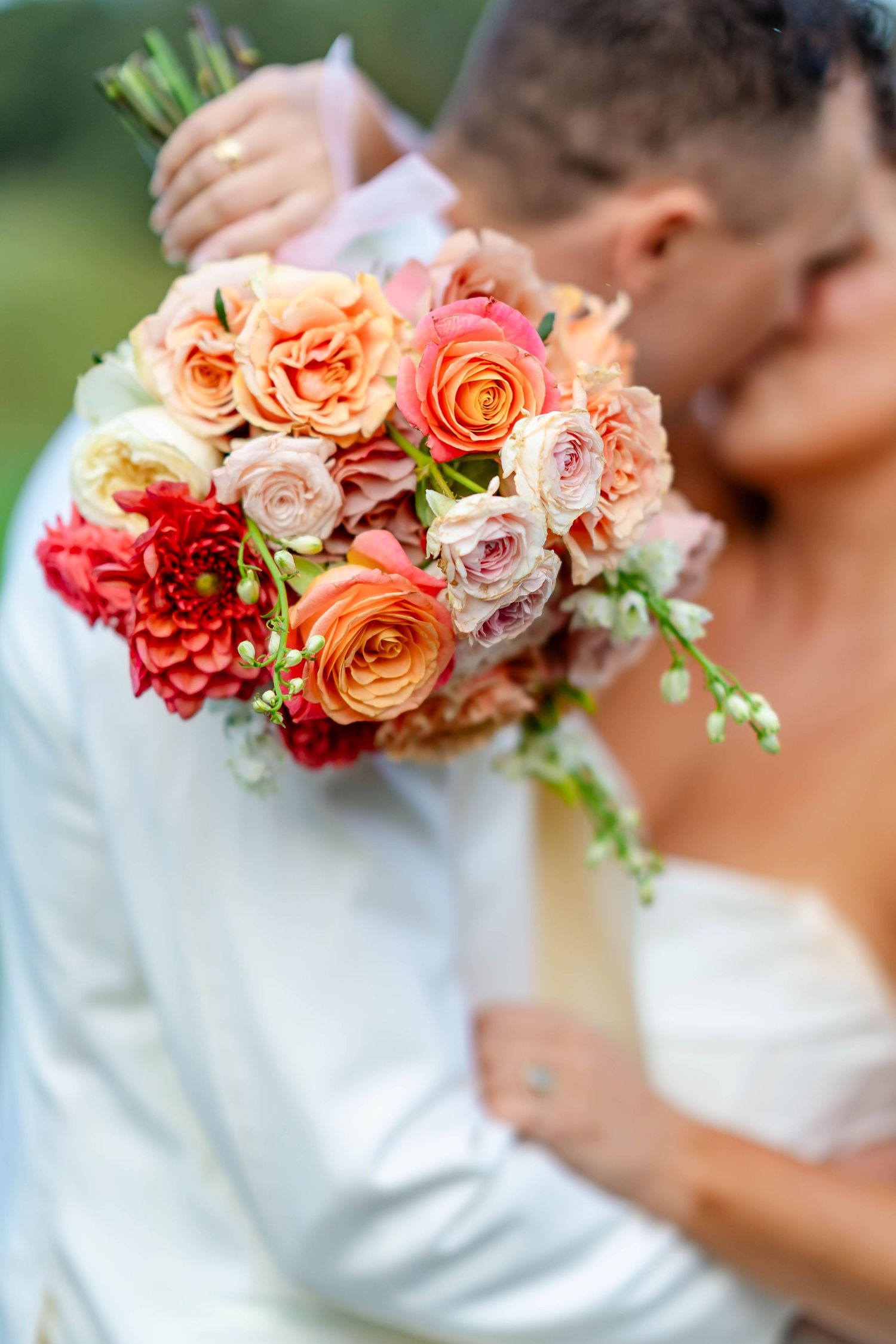Coral and peach roses arranged in a beautiful bridal bouquet against a white wedding dress background.