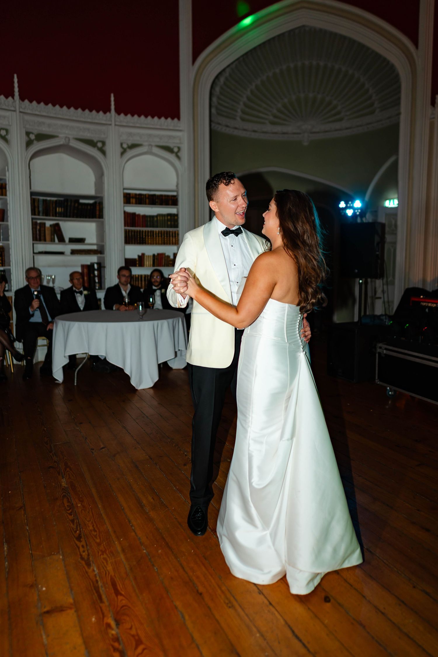 A couple shares their first dance as newlyweds on a polished wooden dance floor in an elegant ballroom.