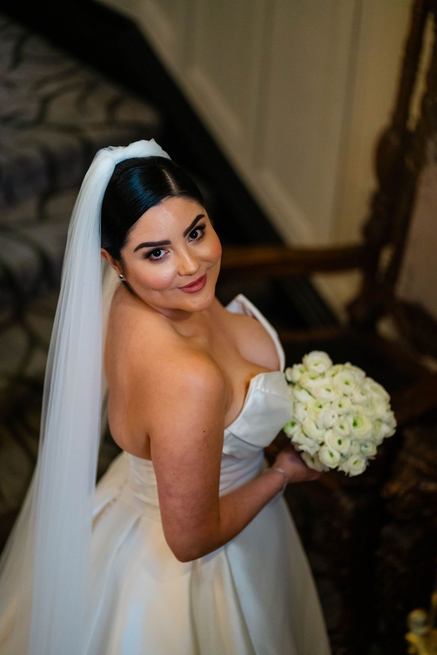 Bride in strapless white gown holds classic white rose bouquet.