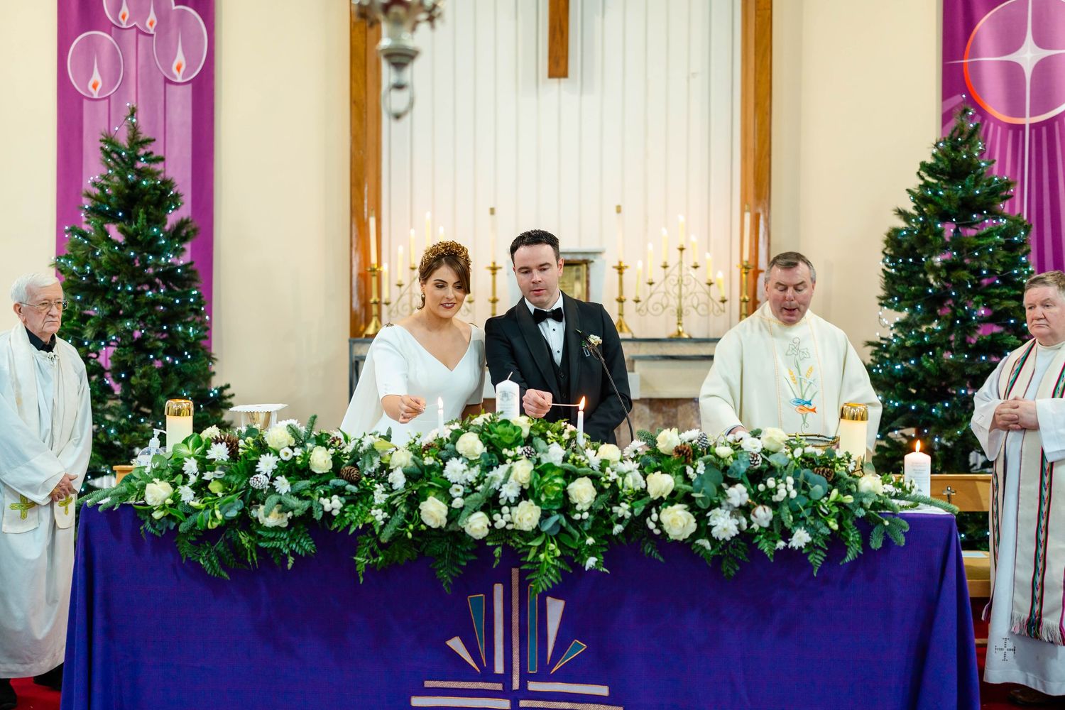Church altar adorned with white floral arrangements and purple banners for a wedding ceremony.