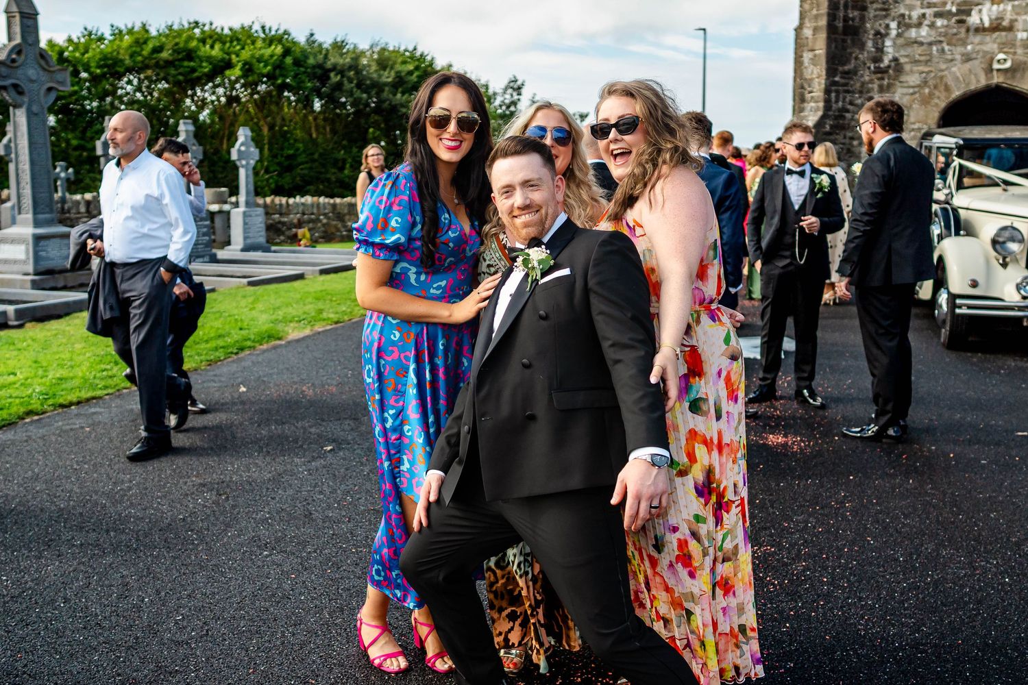 Wedding guests in colorful attire gathered outside a stone building.
