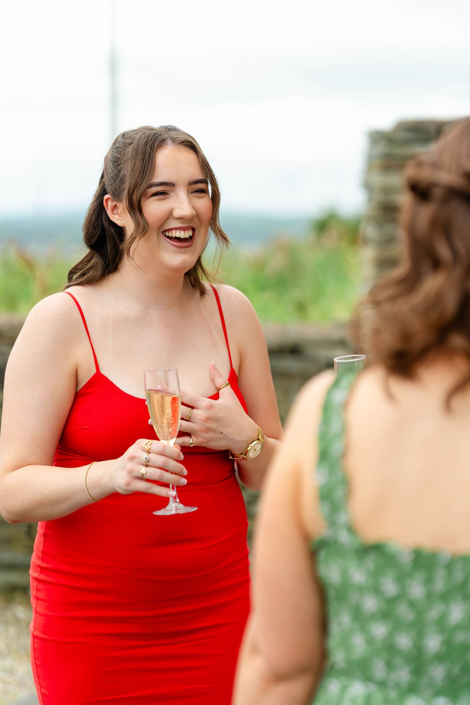 Women in bright red and floral dresses toast with champagne glasses outdoors.