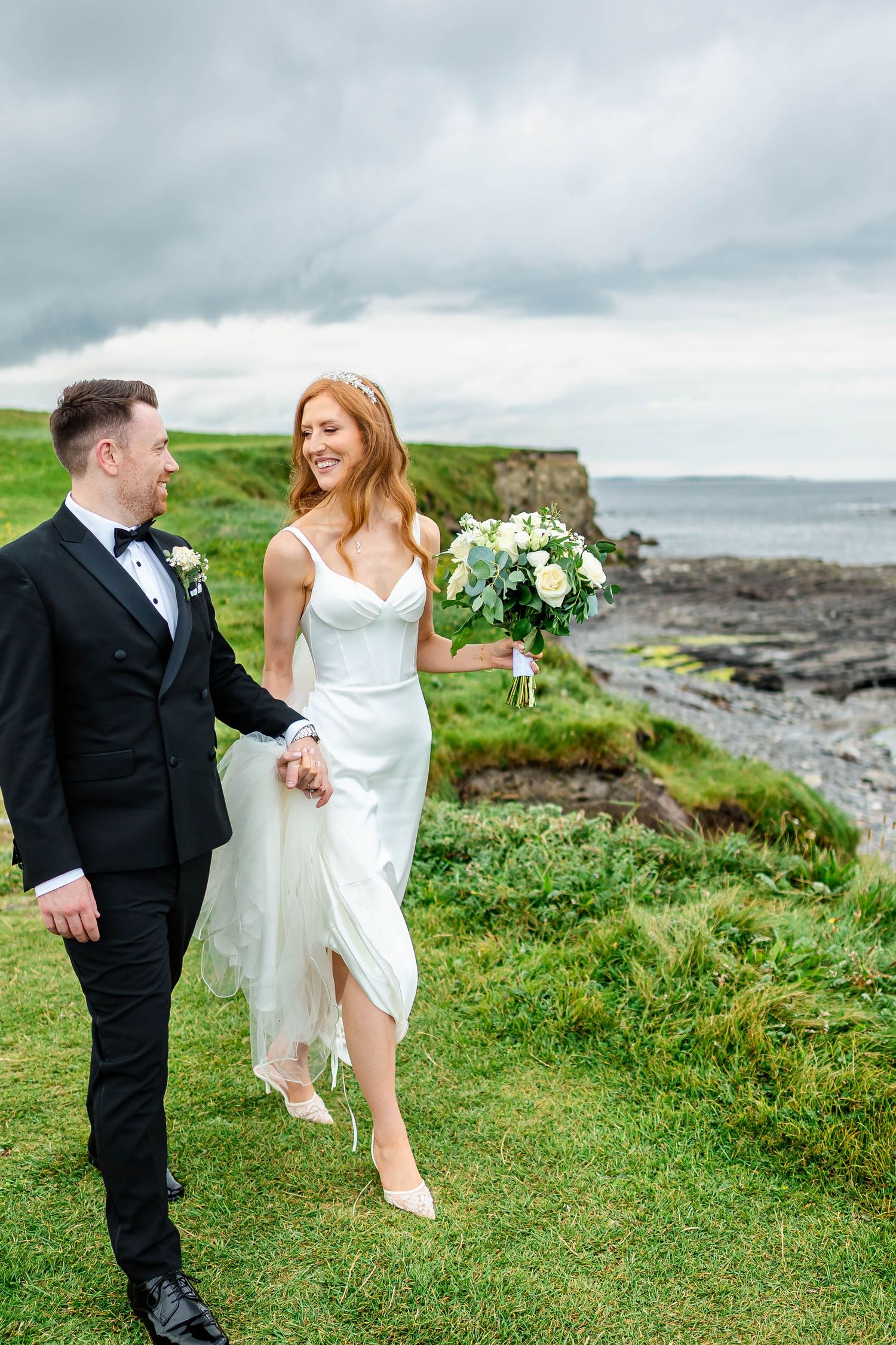 A couple shares joyful moments on their wedding day against a dramatic coastal Irish landscape.