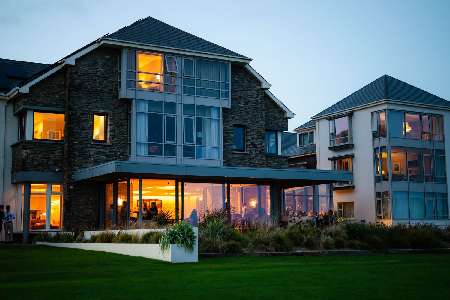 Modern coastal homes with illuminated windows at dusk along a residential development.