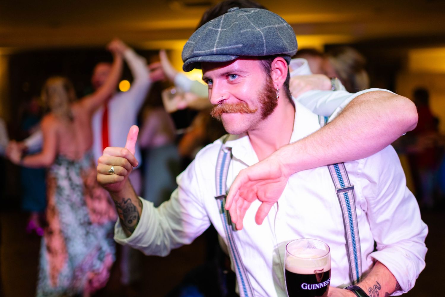 Energetic dancer in flat cap and suspenders moves to the music at wedding reception.