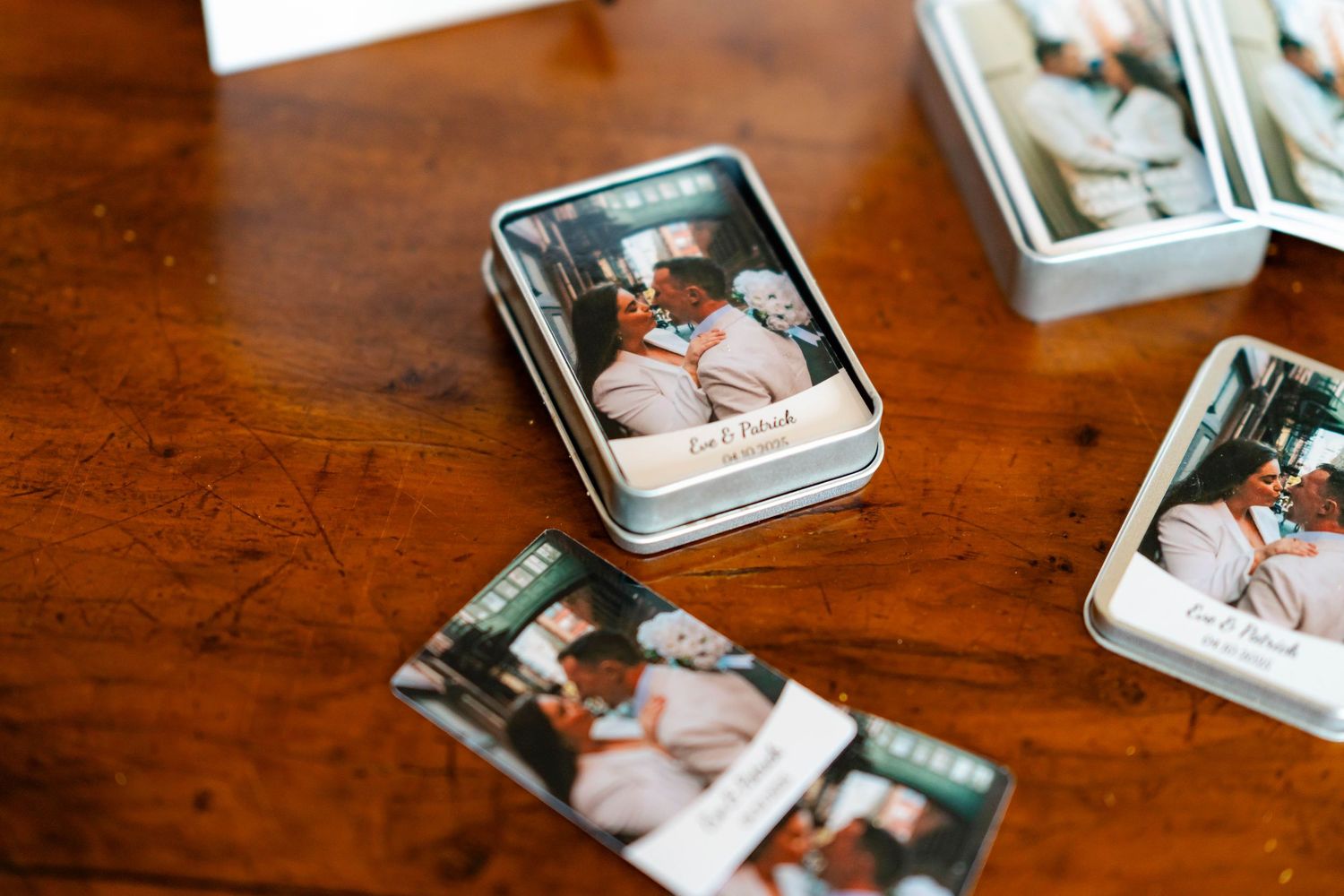 Wedding photos in vintage metal tins scattered across a dark wooden table surface.