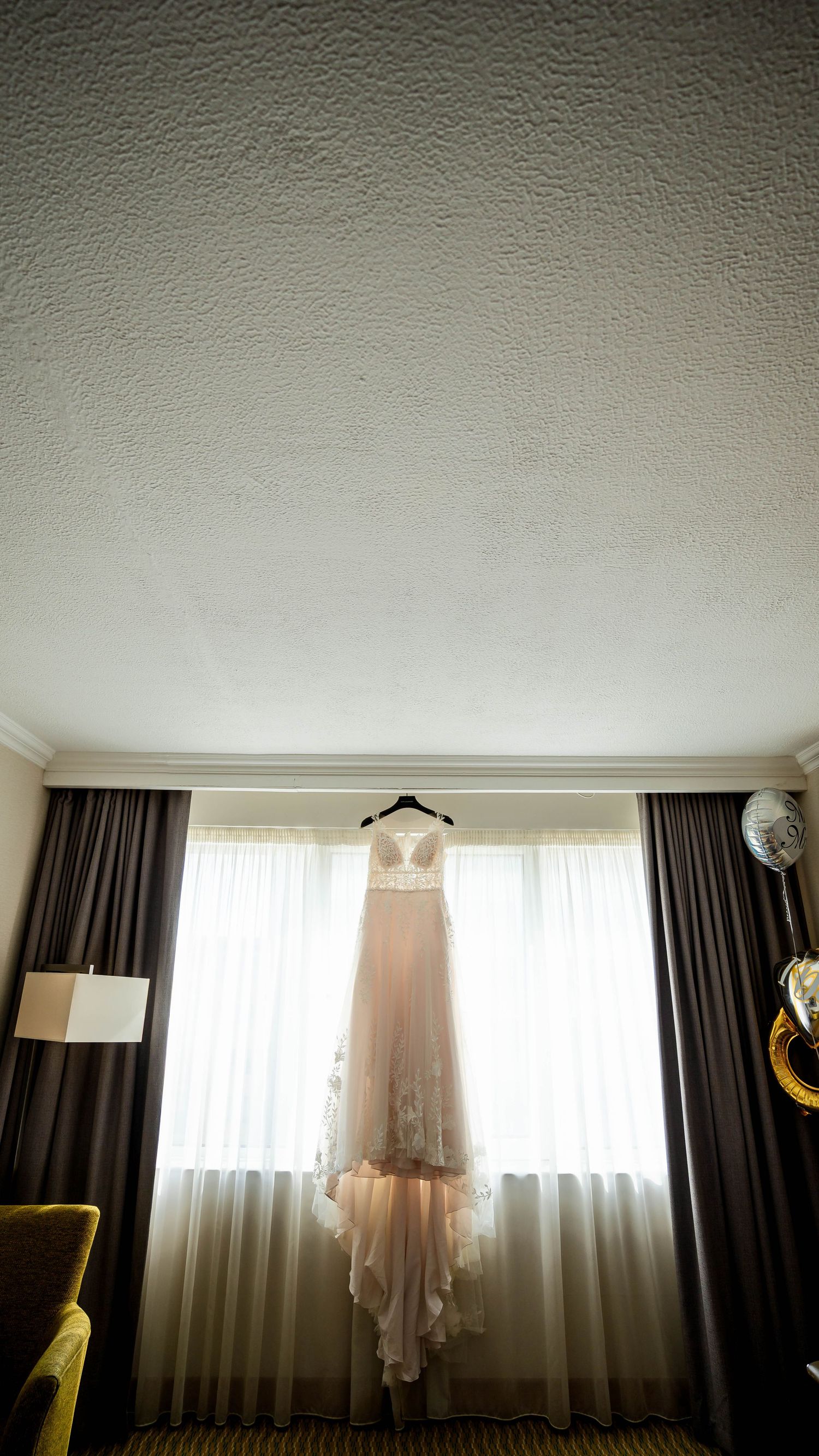 A wedding dress hangs elegantly by a window with natural light streaming in.