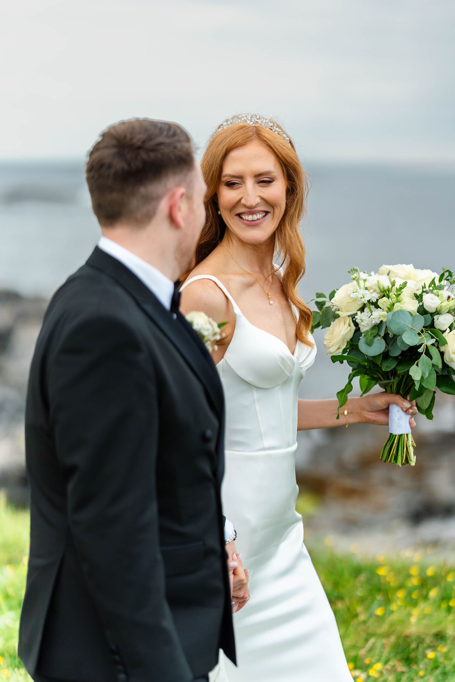 A joyful wedding moment captured on a rocky coastline with a stunning floral bouquet.
