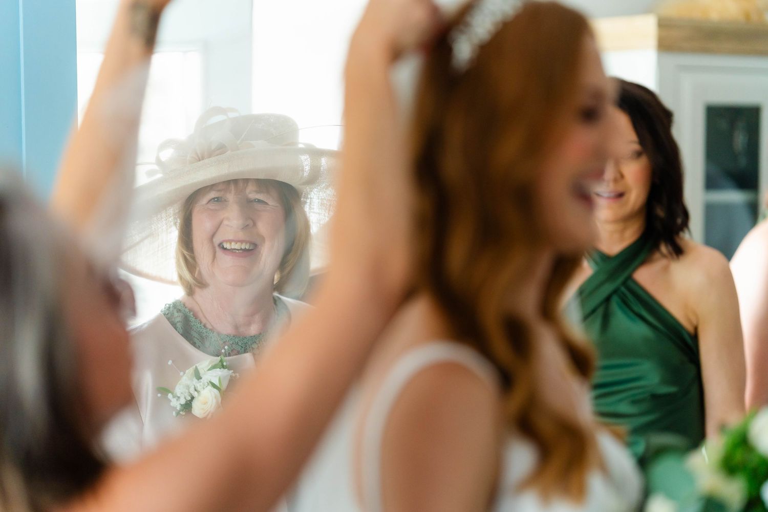 Wedding party wearing emerald green dresses gathered together in a bright indoor setting.