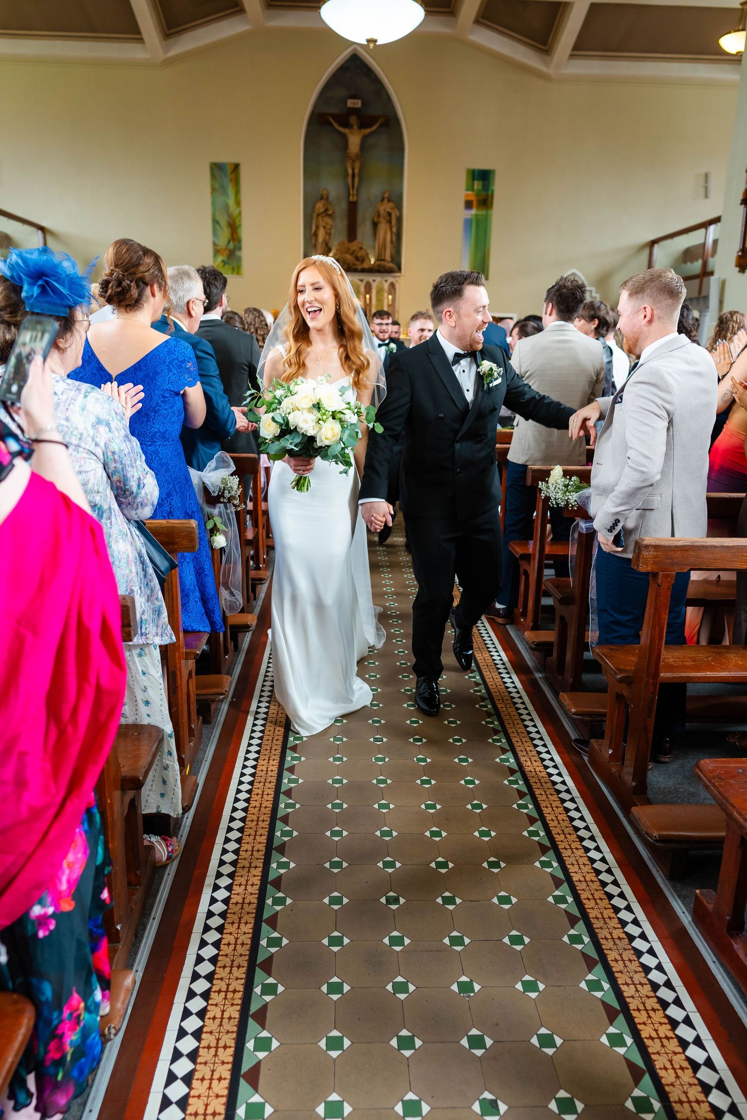 Wedding guests mingling inside a church with decorative tiled floor and wooden pews.