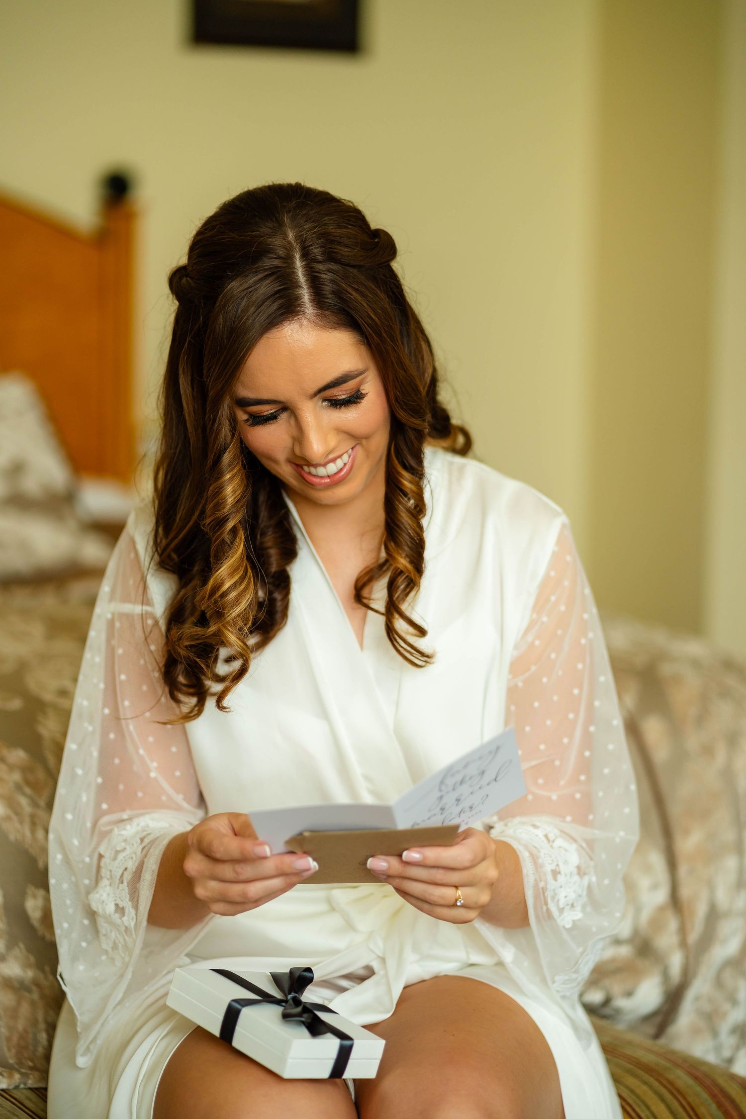 Person in white silk robe reading a letter while sitting on couch.