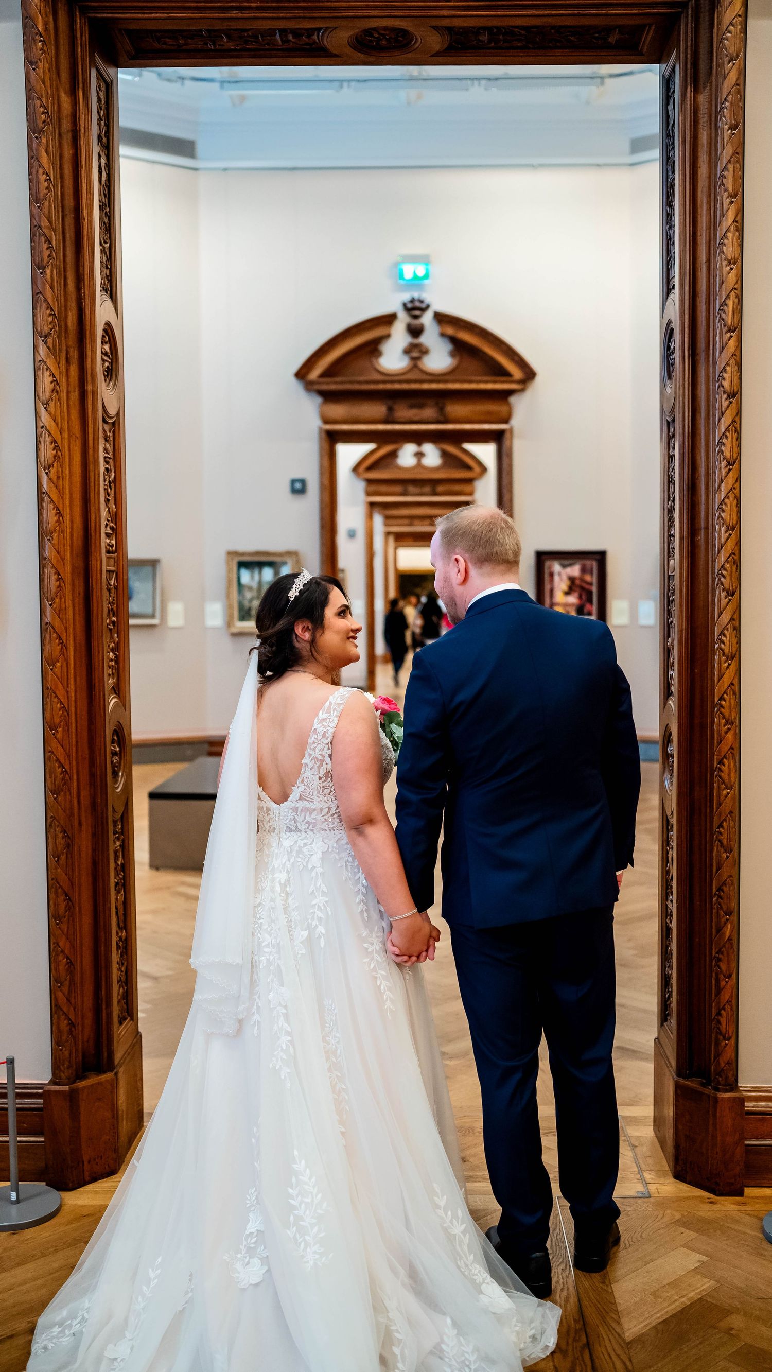Wedding party walking through an elegant wood-paneled gallery room with ornate trim.