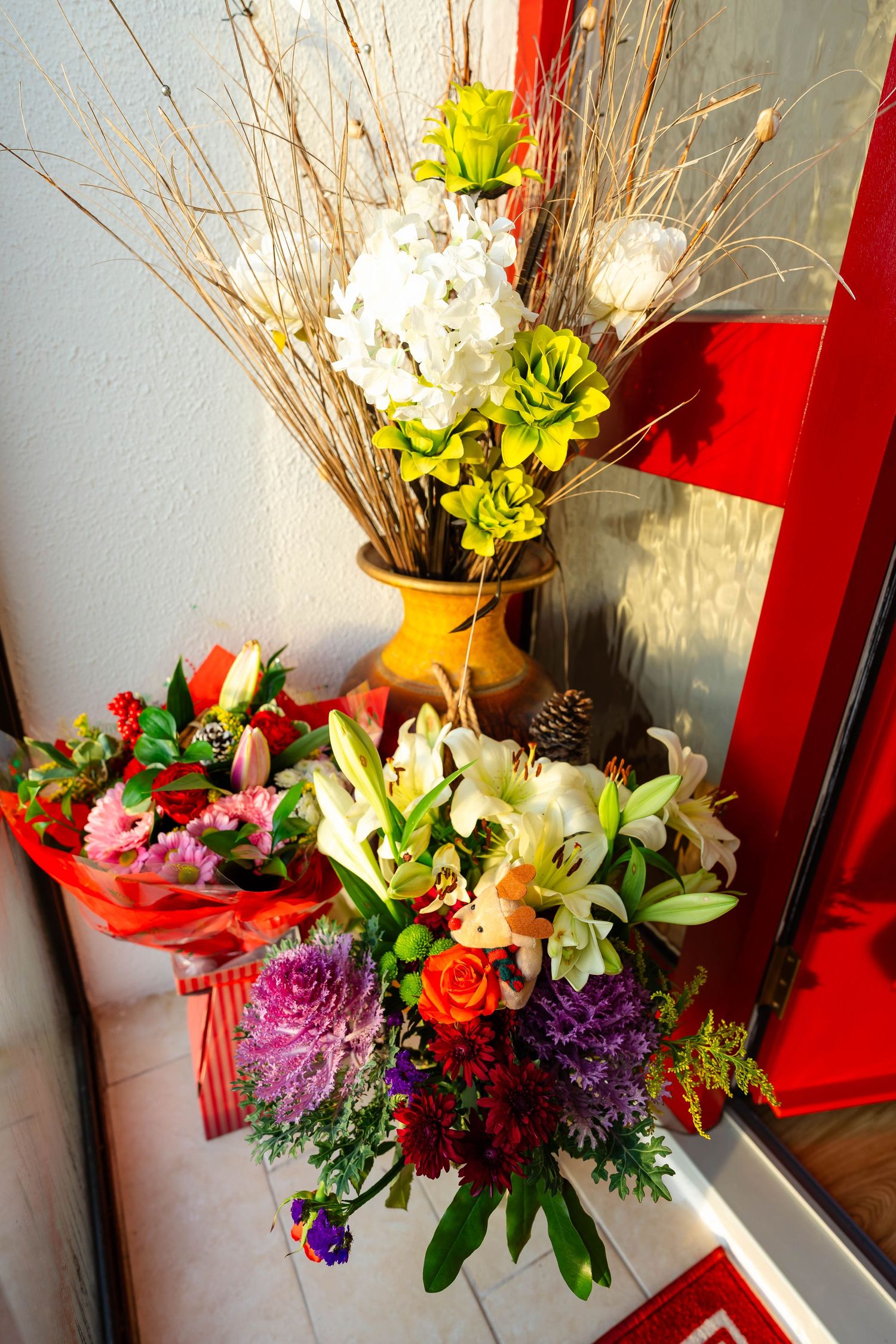 Vibrant floral arrangement with lilies, roses and greenery against a red background.