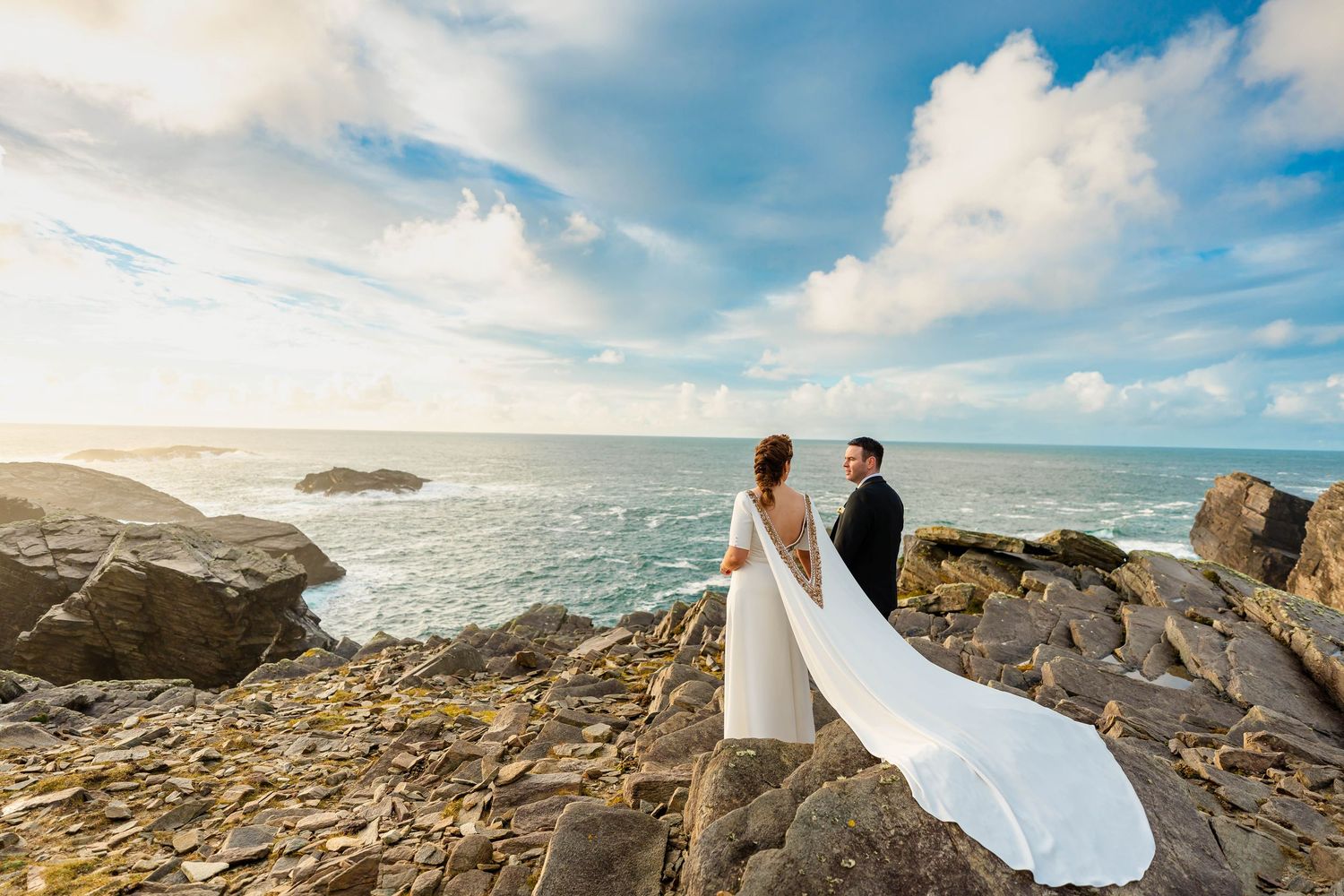 Wedding photography session on rugged coastal cliffs with crashing waves and dramatic sky.