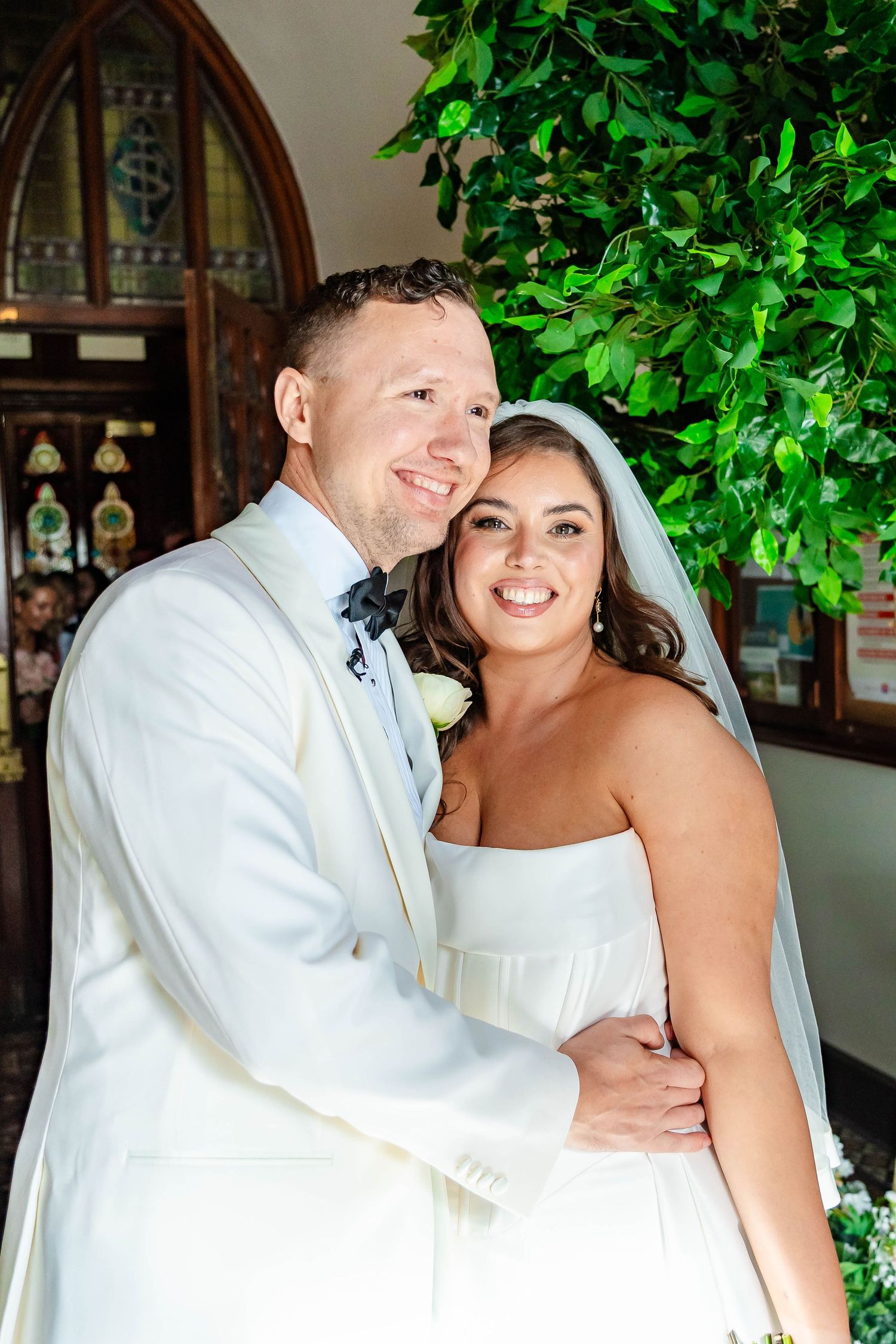 A happy couple shares joyful moments in their wedding attire against a backdrop of green foliage.