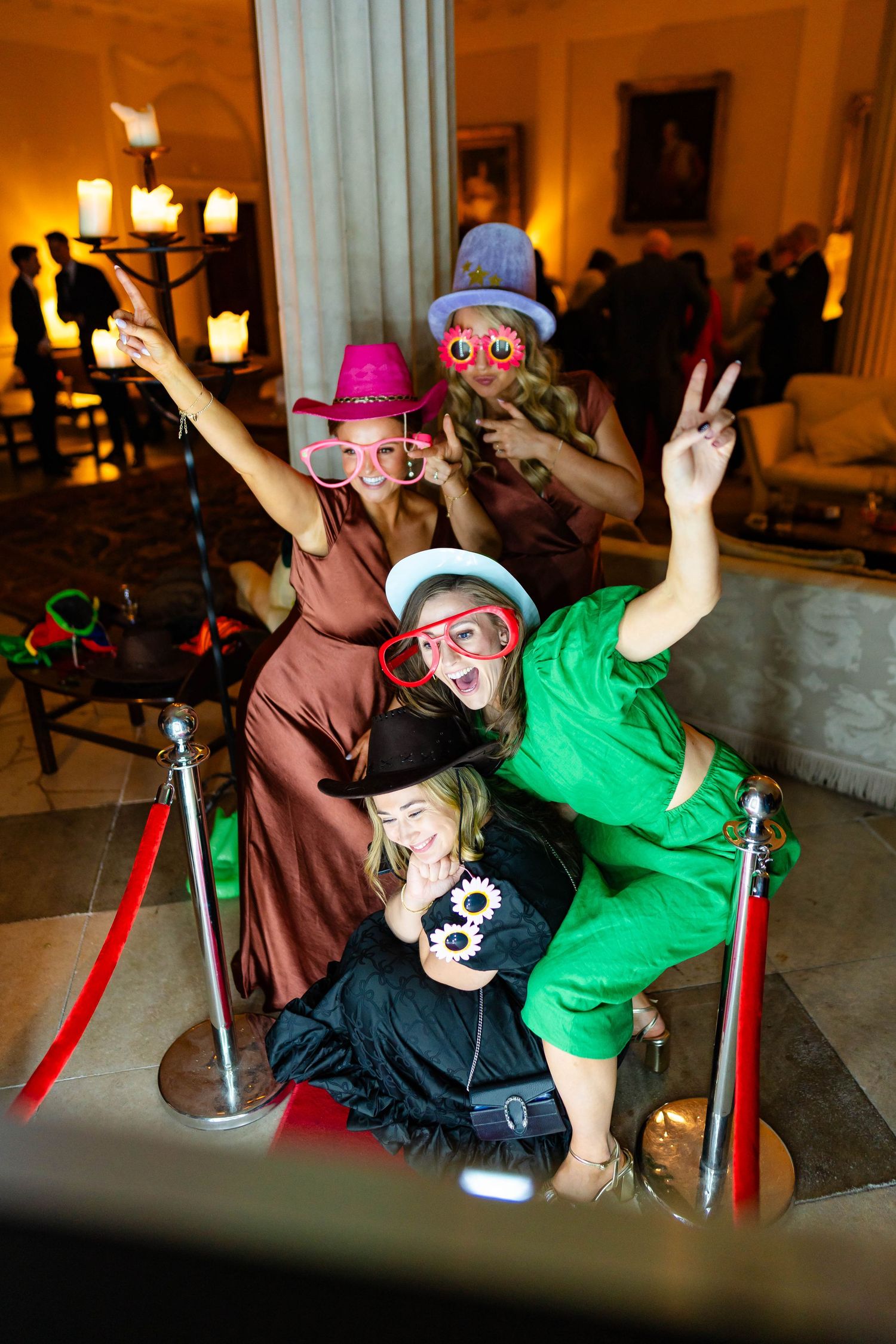 Two friends in colorful outfits strike playful poses while lounging on a couch at an indoor venue.