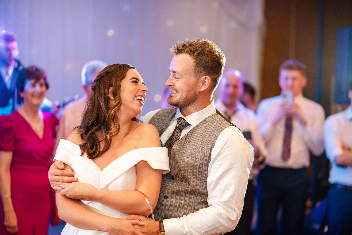Couple dances together at reception with purple lighting and festive atmosphere.