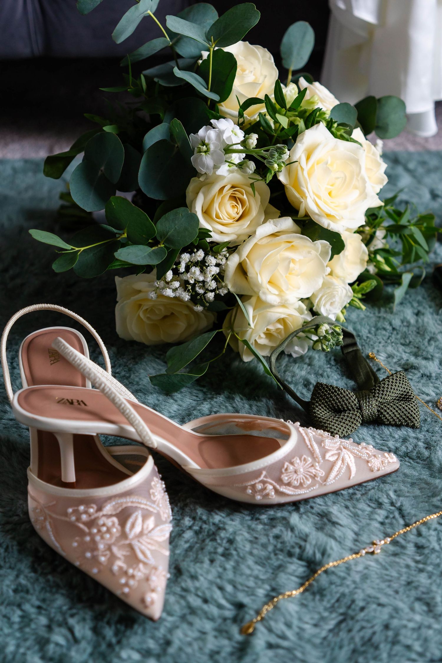 Elegant bridal shoes with pearl details next to white roses and eucalyptus.
