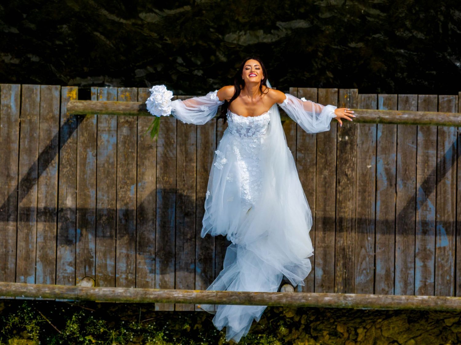 Playful scene of a white dress flowing against rustic wooden fence panels.