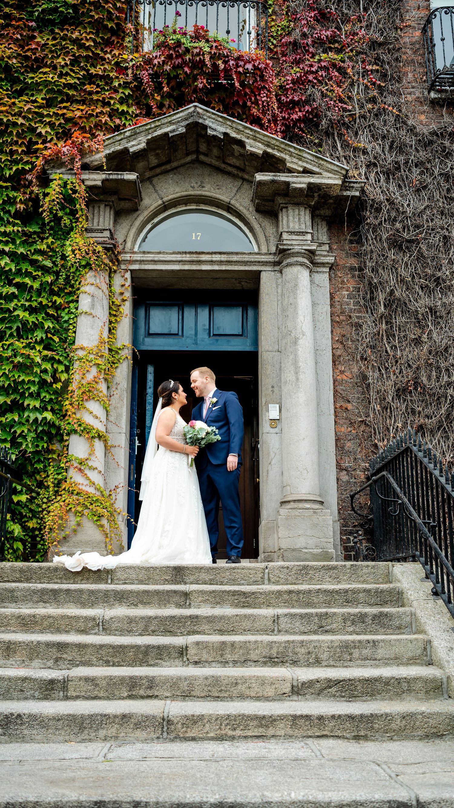 Wedding portraits at historic stone building entrance with ivy-covered walls and blue door.
