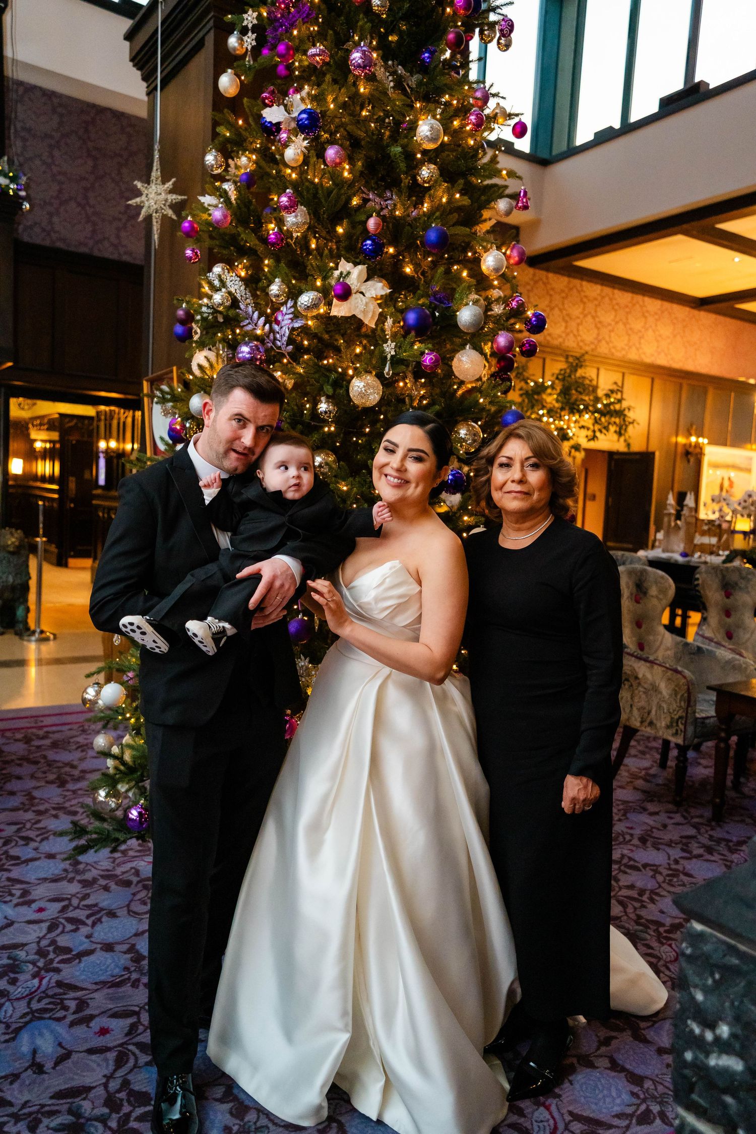 Wedding party poses in front of a decorated Christmas tree during holiday season celebration.
