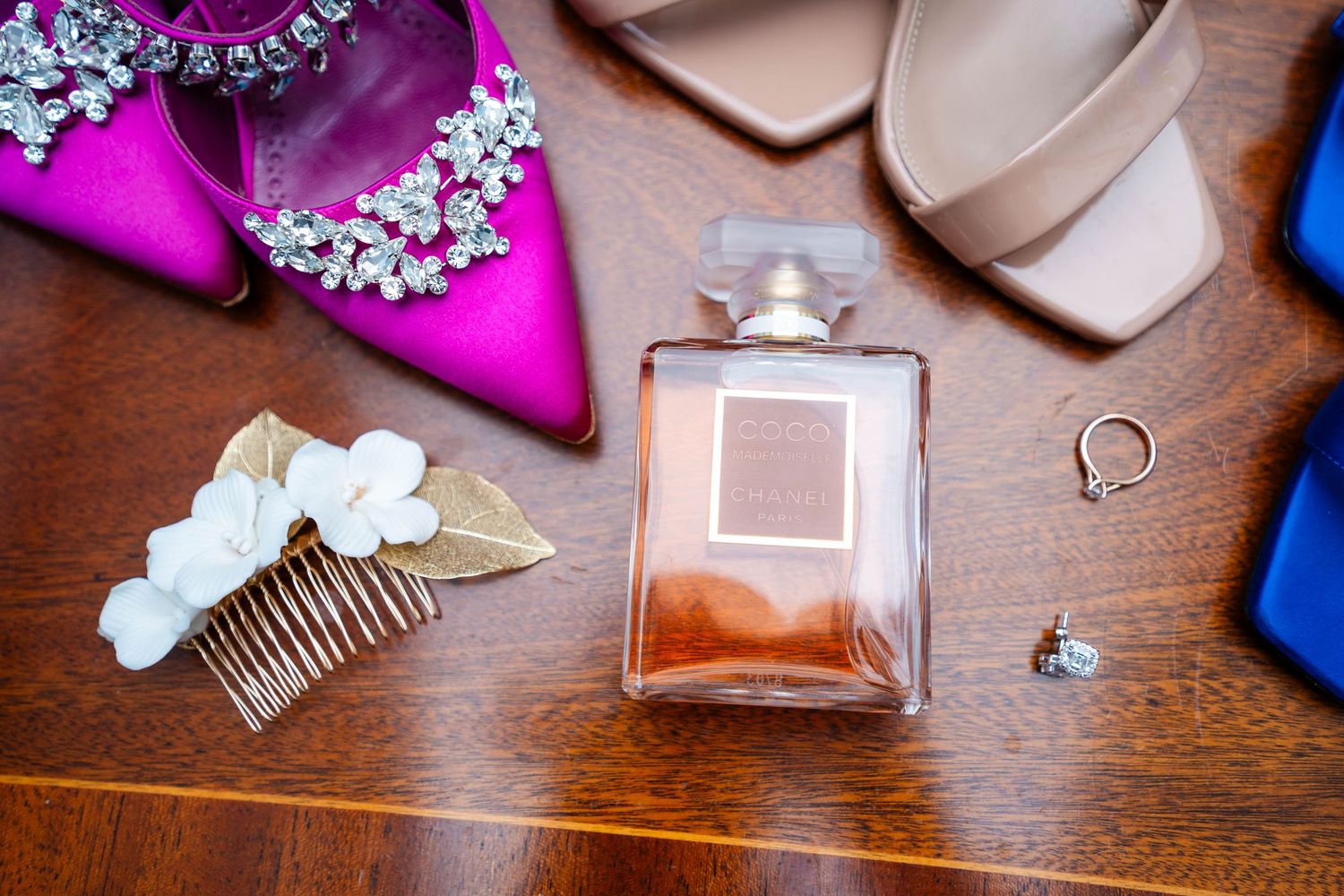 Wedding details including perfume, jewelry, and pink satin shoes arranged on wooden surface.