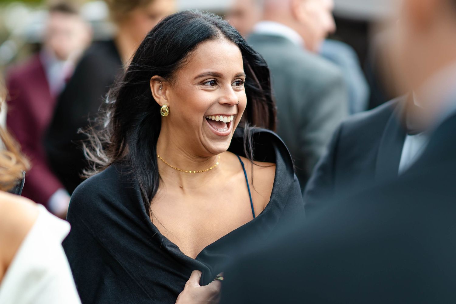 A candid moment at a social gathering shows someone laughing joyfully while wearing a black top.
