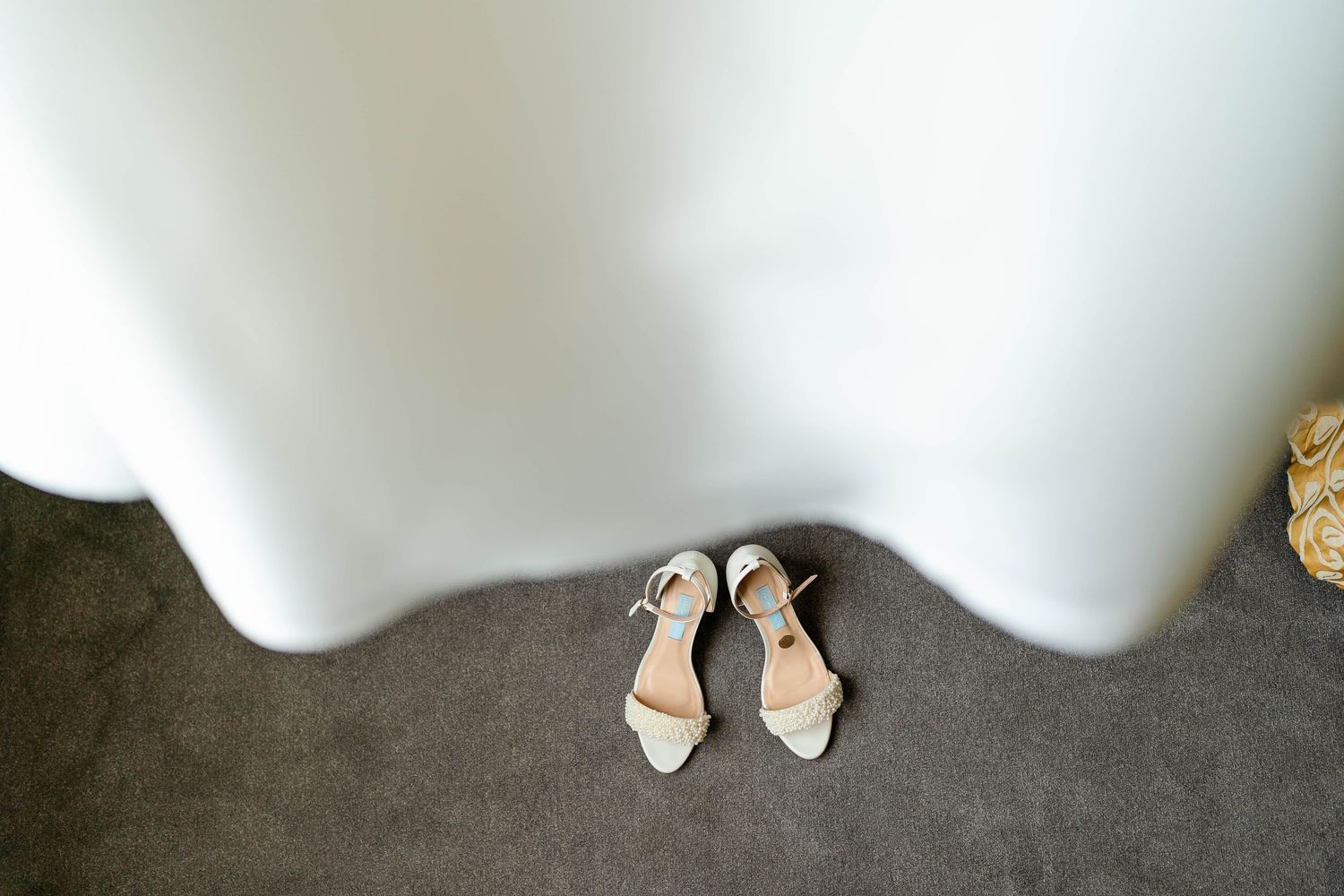 White bridal shoes displayed beneath flowing wedding dress fabric.