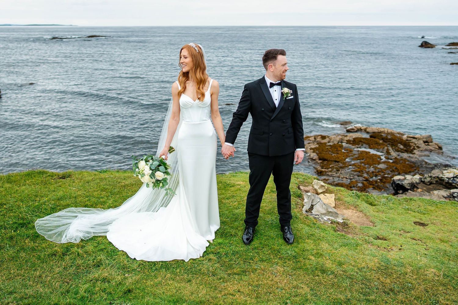 Dramatic coastal wedding portrait with rocky shoreline and ocean backdrop.